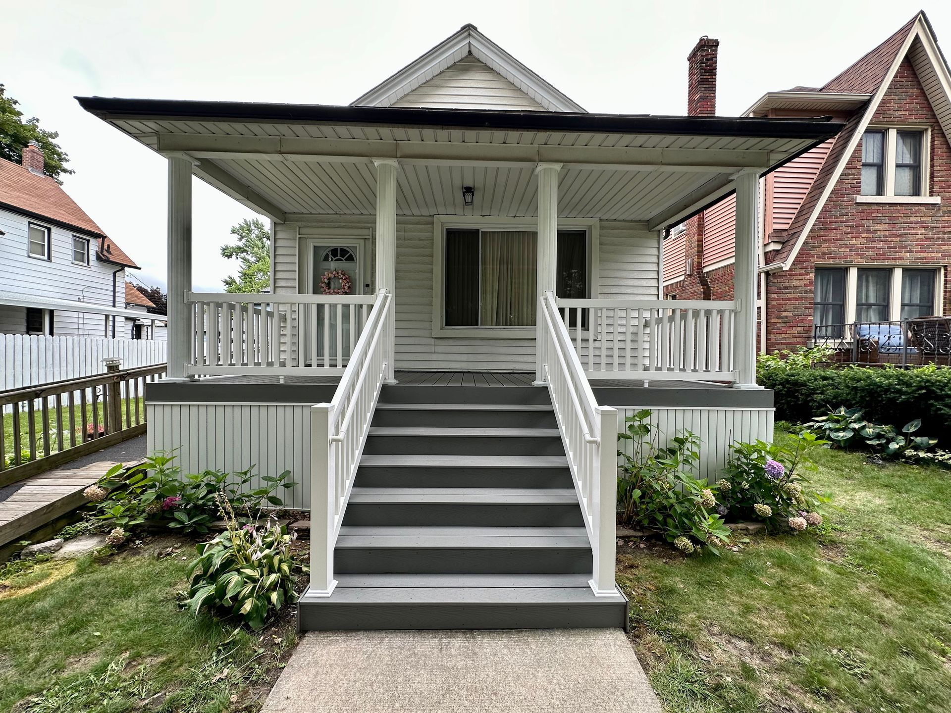 White house with porch and steps, surrounded by grass and other houses.
