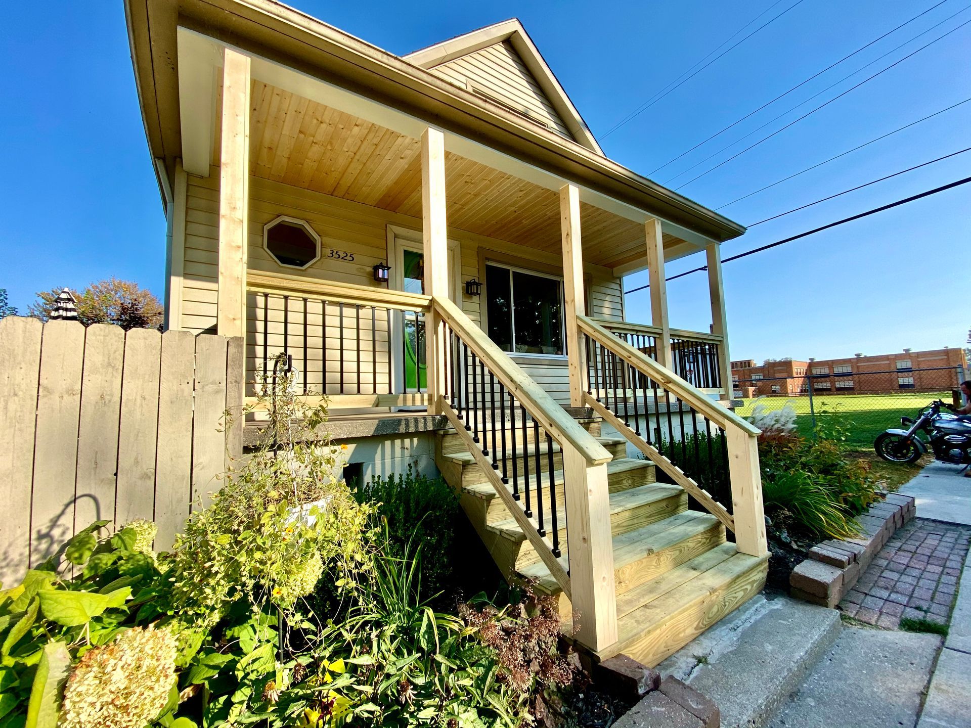 Wooden house with porch and stairs, green door, black railing, blue sky.