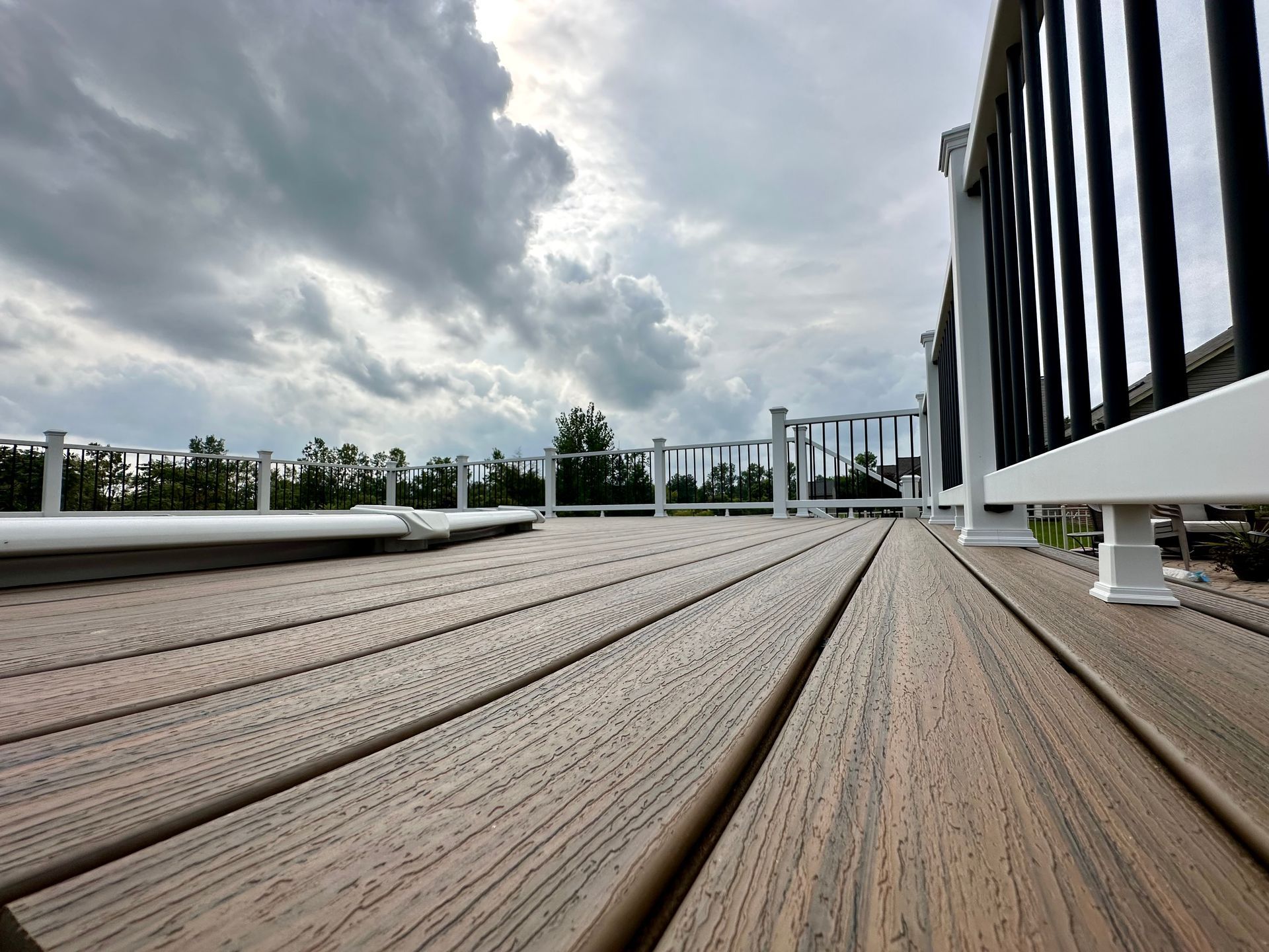 View of a composite deck with black and white railing under a cloudy sky.