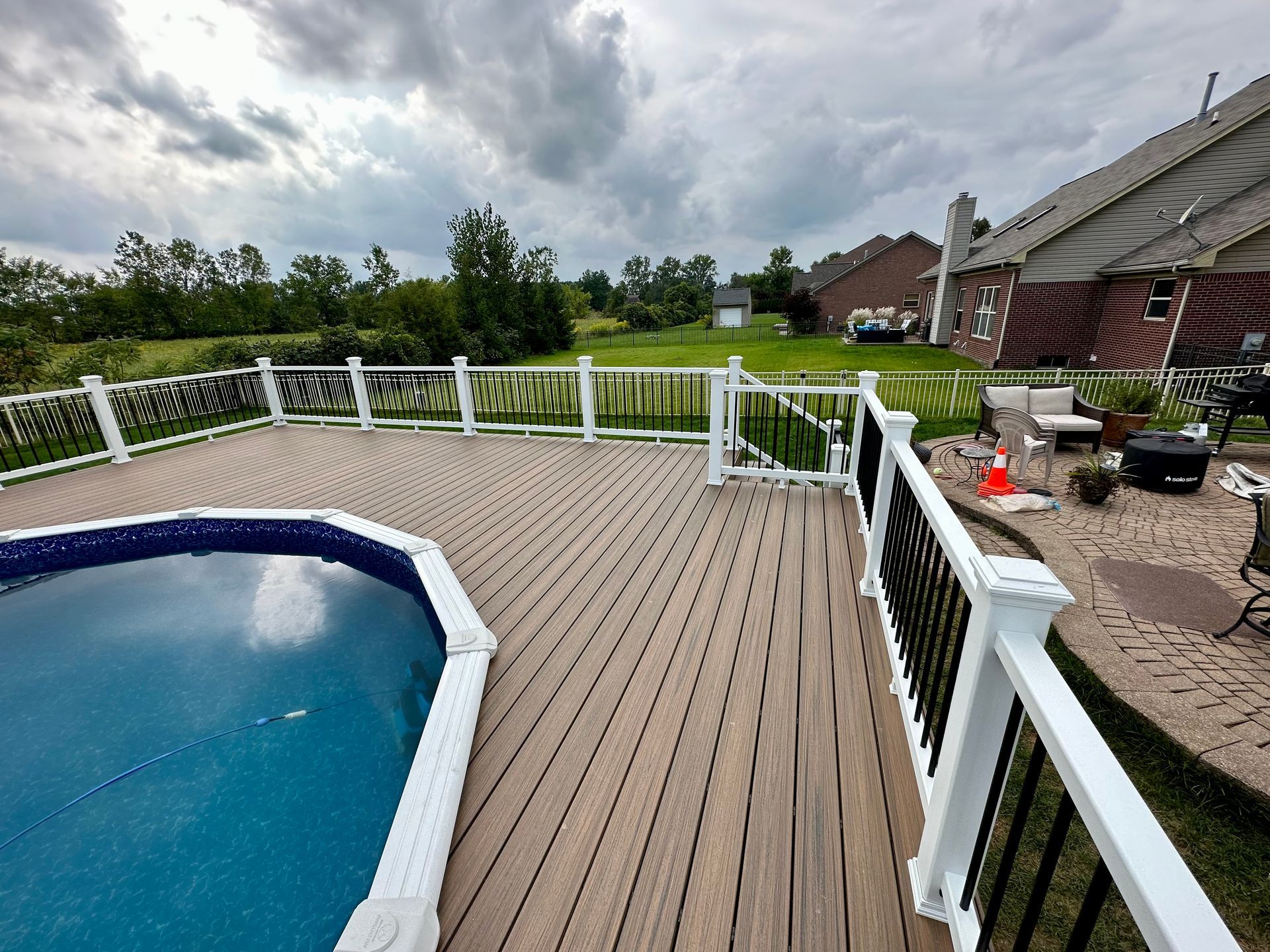 Deck with above-ground pool and white railing, overcast sky, suburban backyard.