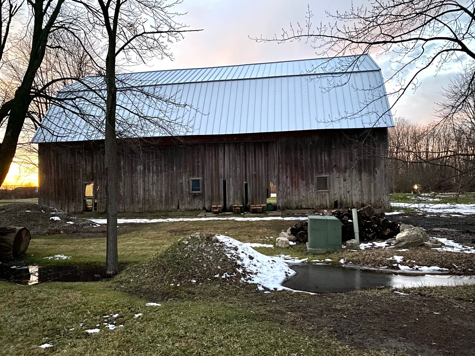 Weathered wooden barn with metal roof against a dusk sky; snow on the ground.
