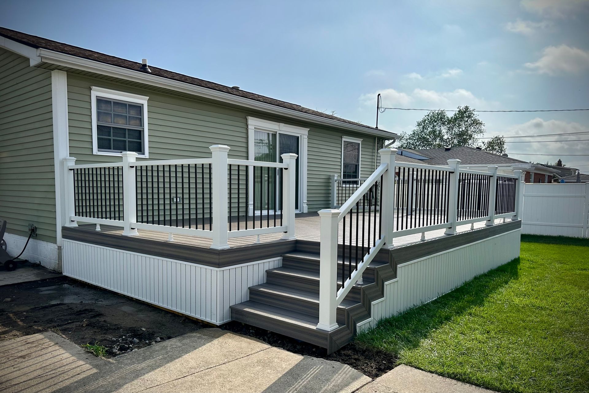 A newly built deck attached to a house with black and white railings and stairs, green siding.