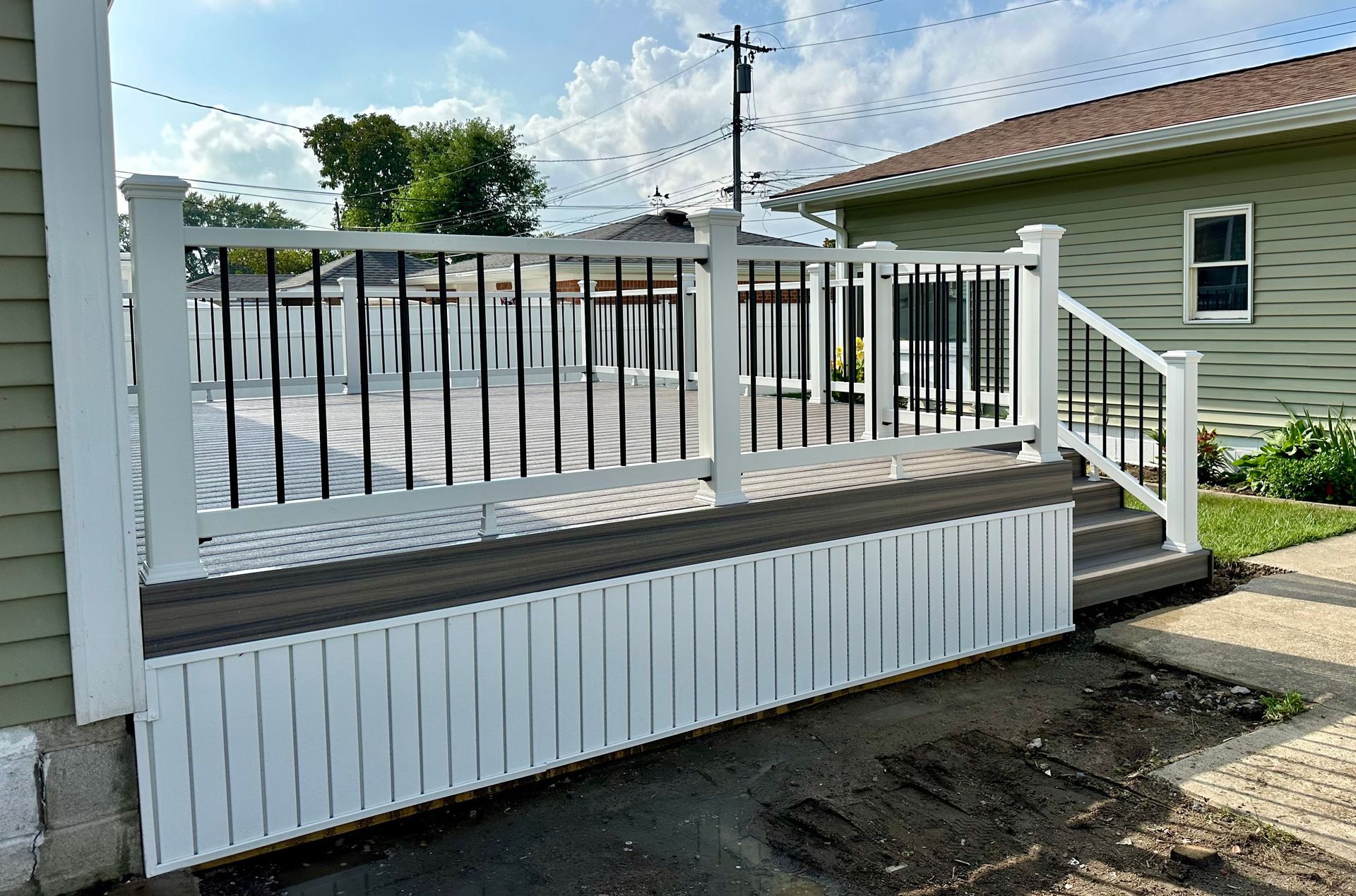 White and black deck with railings attached to a light green house, outdoors.