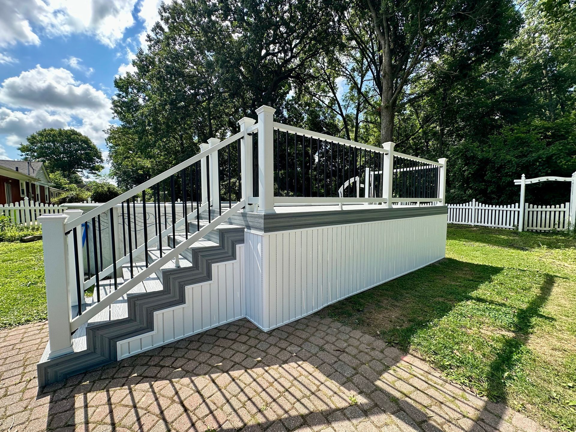 White deck with gray steps and black railings in a grassy backyard, blue sky in the background.