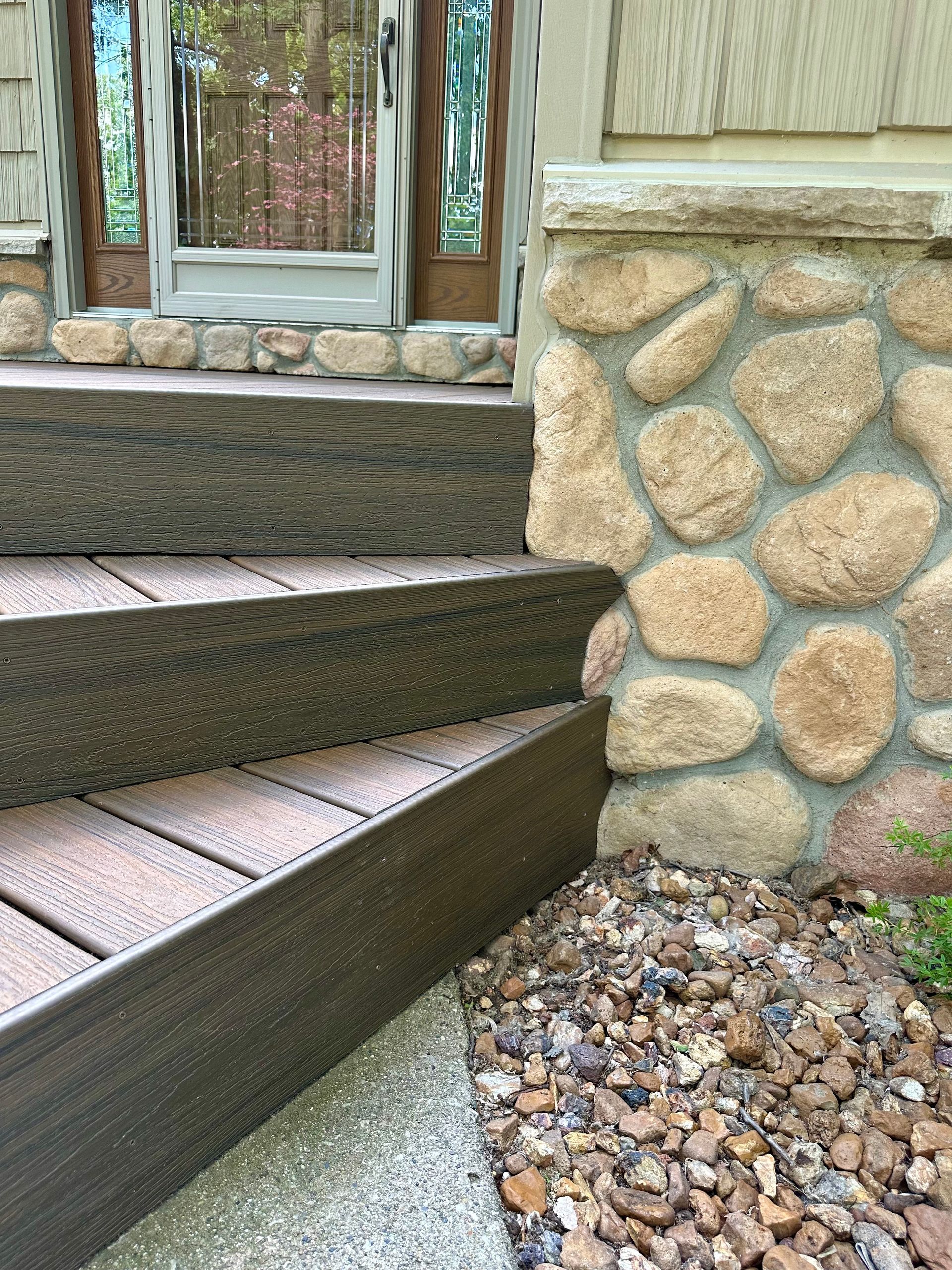 Stone and composite steps leading to a doorway, alongside a stone wall and gravel ground cover.