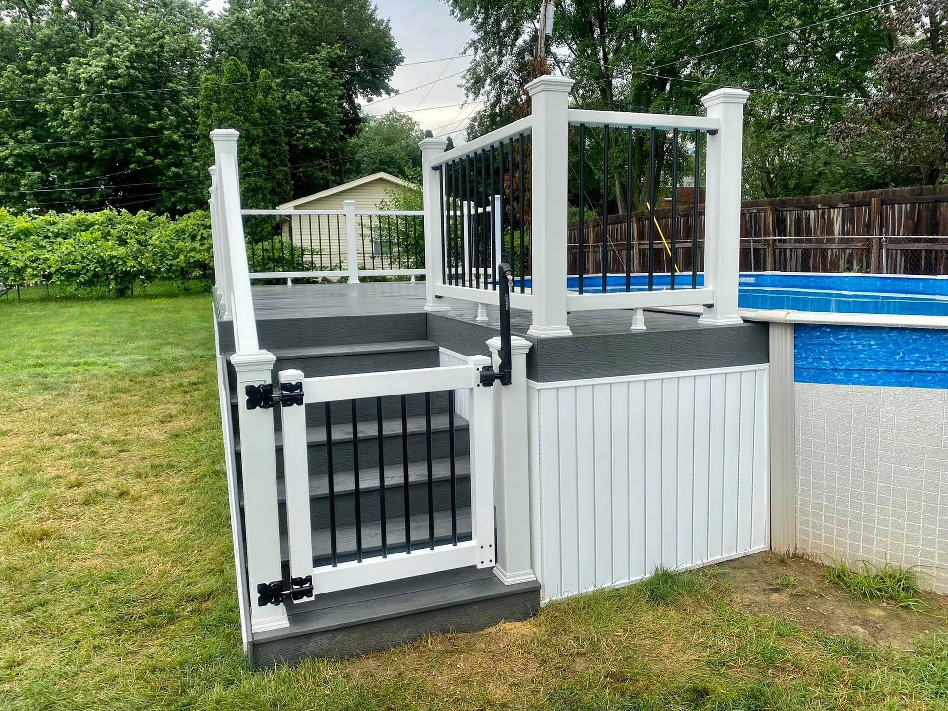 Deck with gate and black railing leading to an above-ground pool in a backyard.