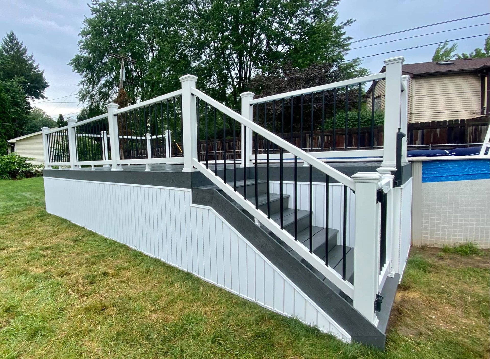 Deck with white railing and black spindles, stairs, and a skirted base, next to a pool.