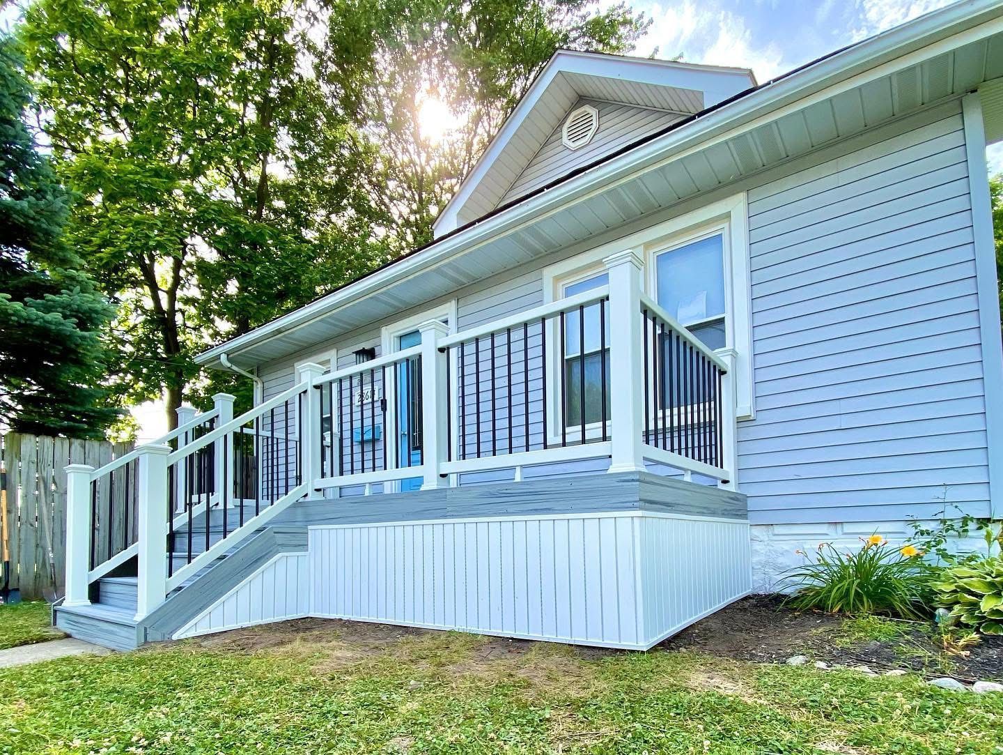 Light blue house with a gray deck and white railing, sunny outdoor setting.