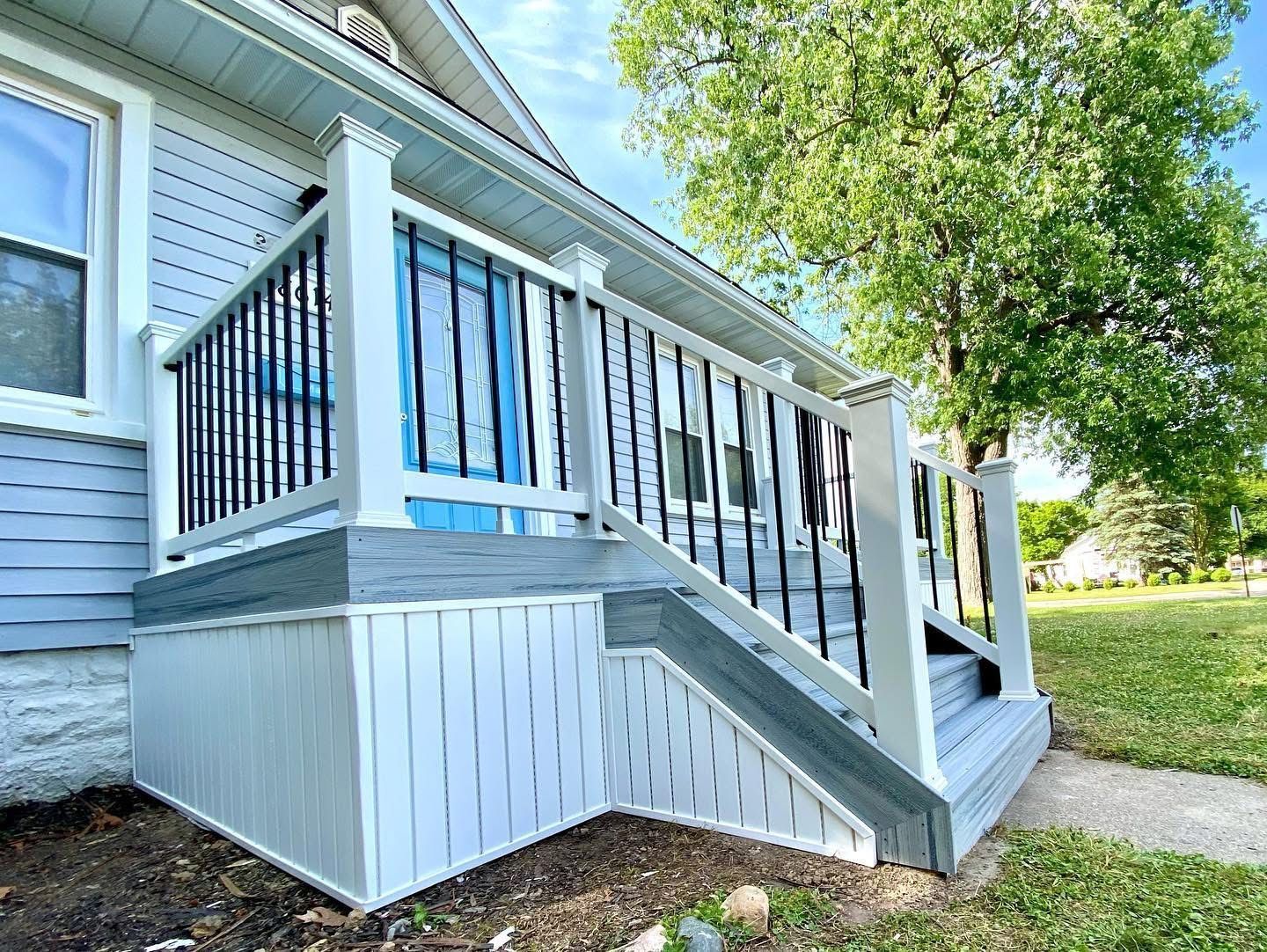 Newly renovated front porch with gray and white paint, black railing, and blue door.