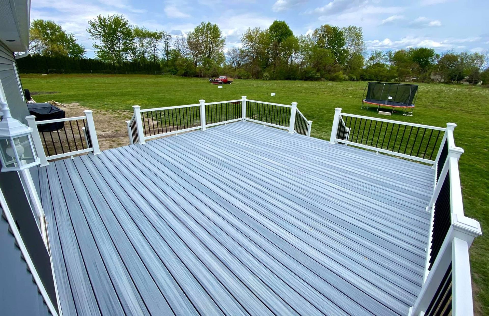 A gray composite deck with white railings and black balusters overlooks a green lawn and trees.