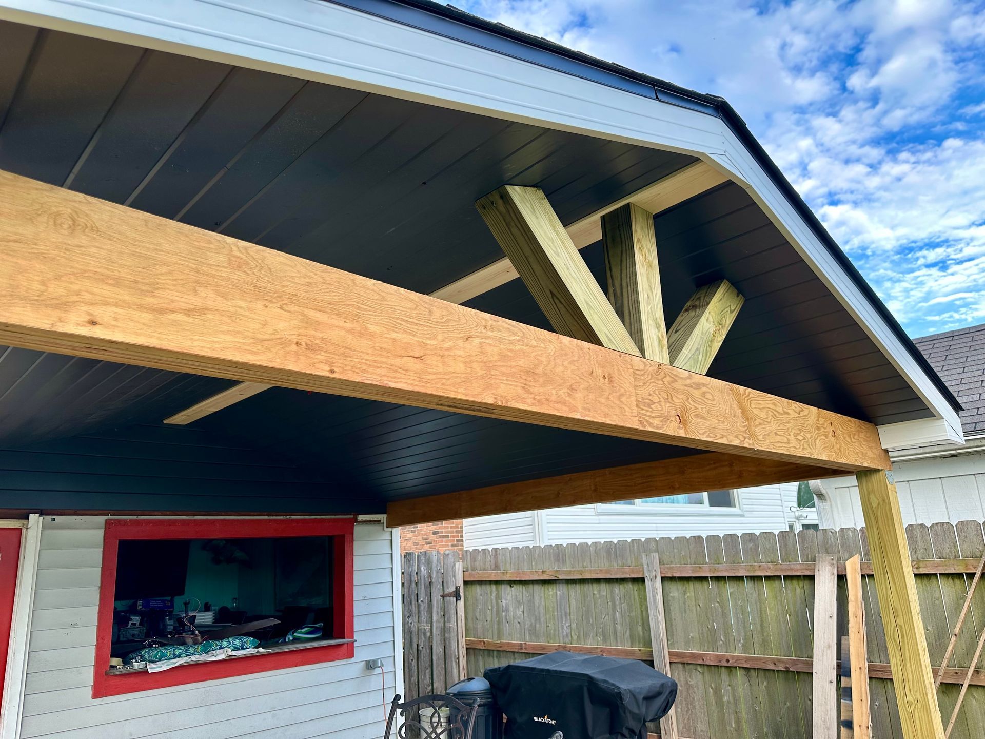 Wooden beam construction of a covered outdoor structure. Dark ceiling and trim; light wood support.