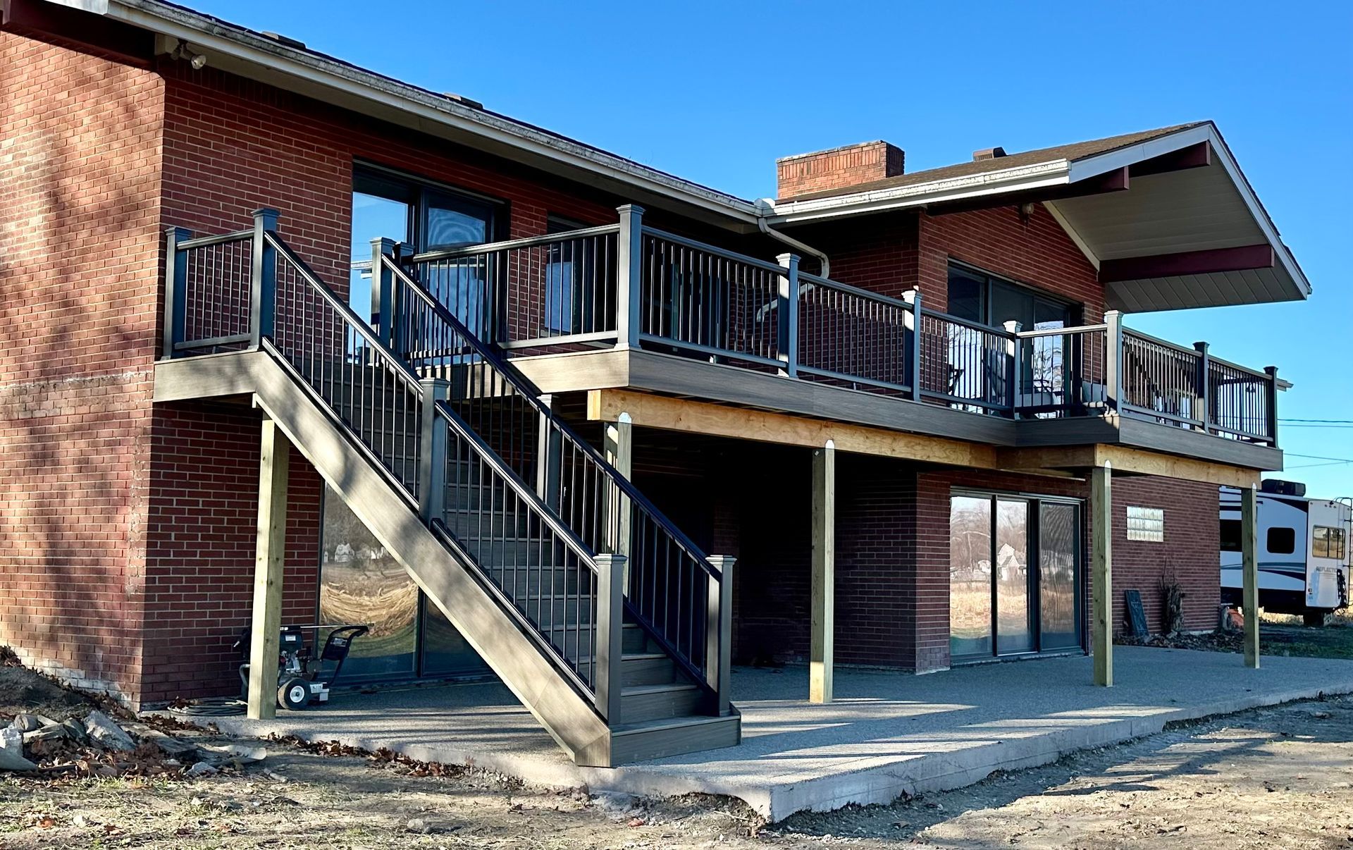 Two-story brick building with a wooden deck and stairs, with a concrete patio.