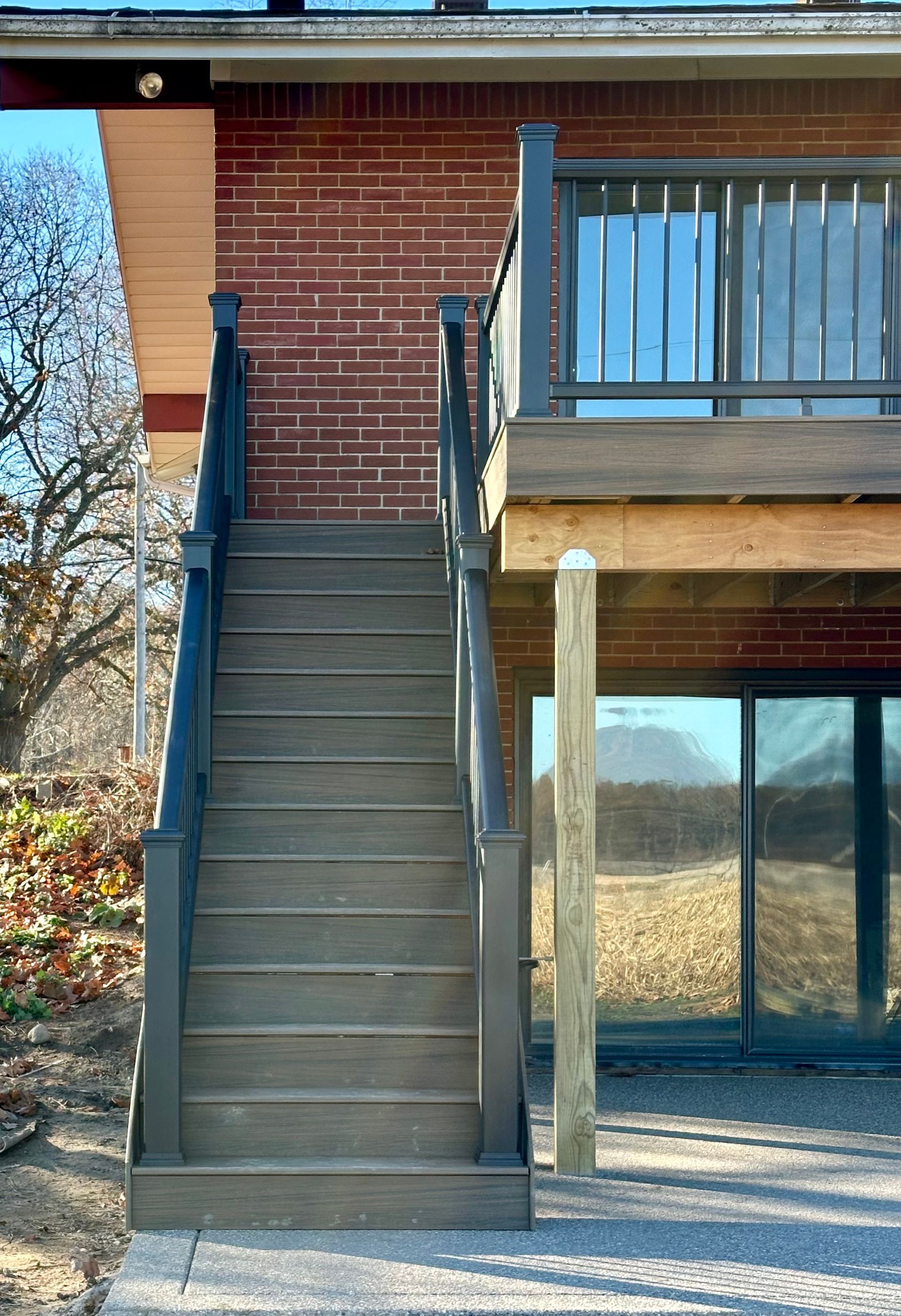 Exterior stairs leading up to a deck with dark gray railings and brick building background.