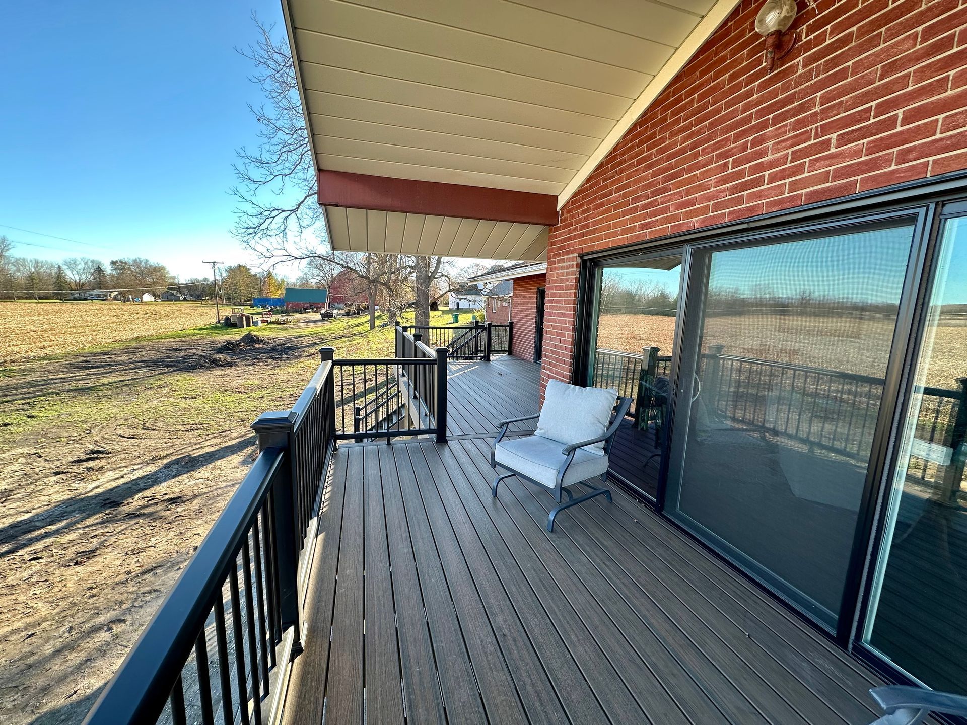 Deck of a brick house overlooking a field. A chair sits by sliding glass doors.