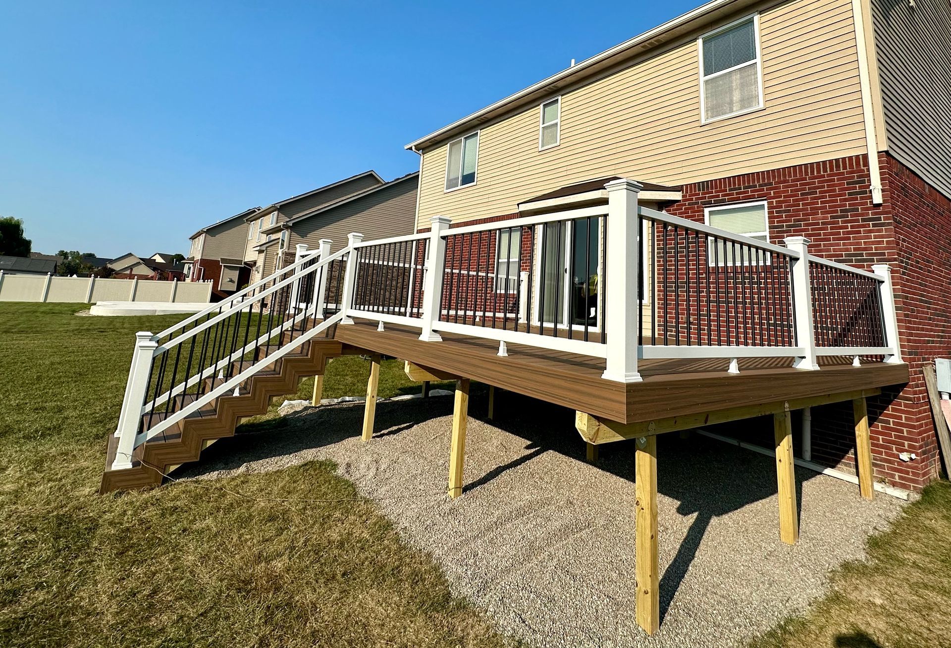Deck attached to a two-story brick house with white railing and stairs. Gravel ground cover in backyard.
