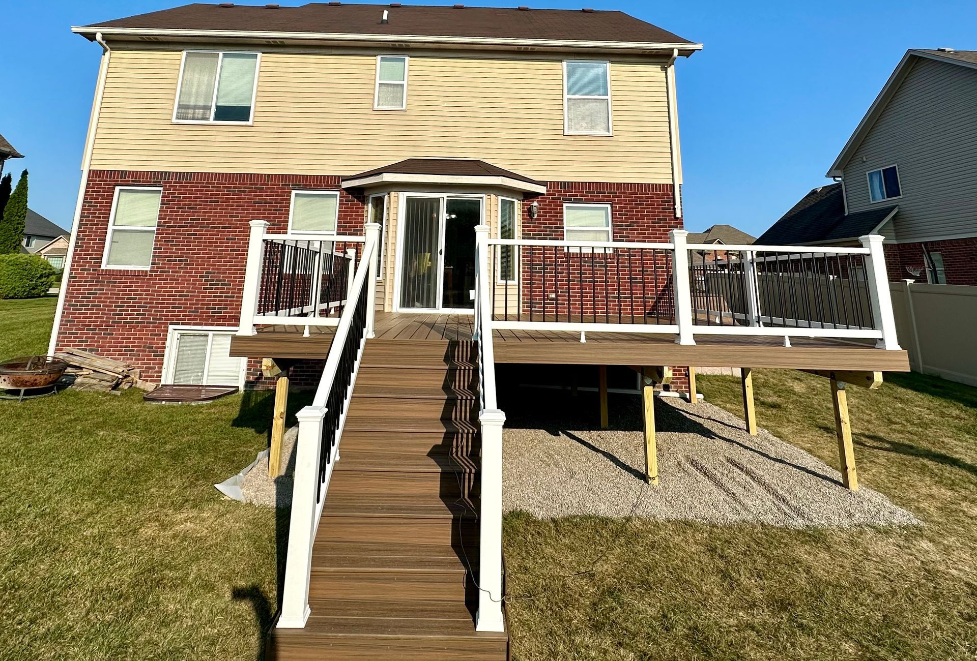 Back of a two-story house with a wooden deck, stairs, and gravel base; backyard setting.