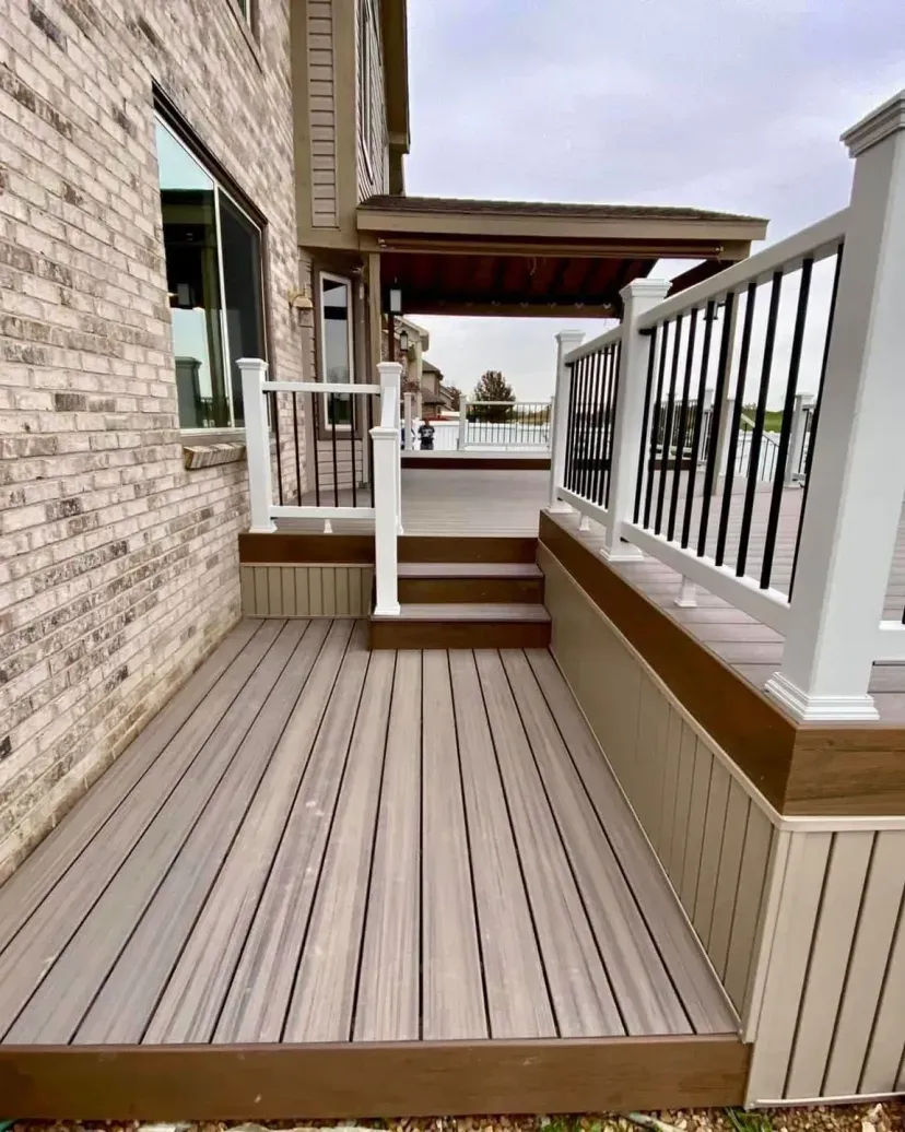 A wooden deck with a white railing and stairs next to a brick building.