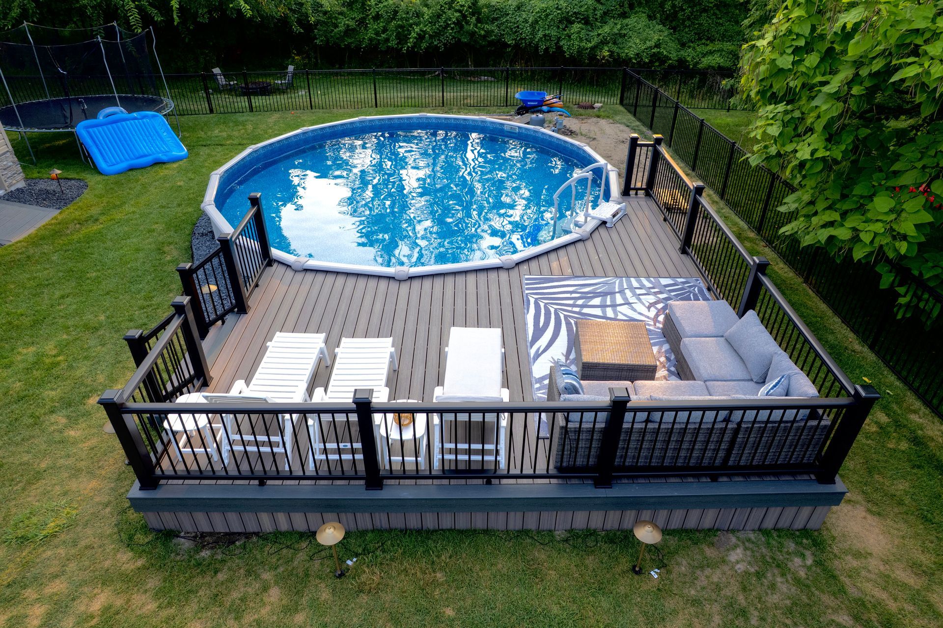 Above-ground pool with attached deck featuring lounge chairs, a seating area, and a fence.