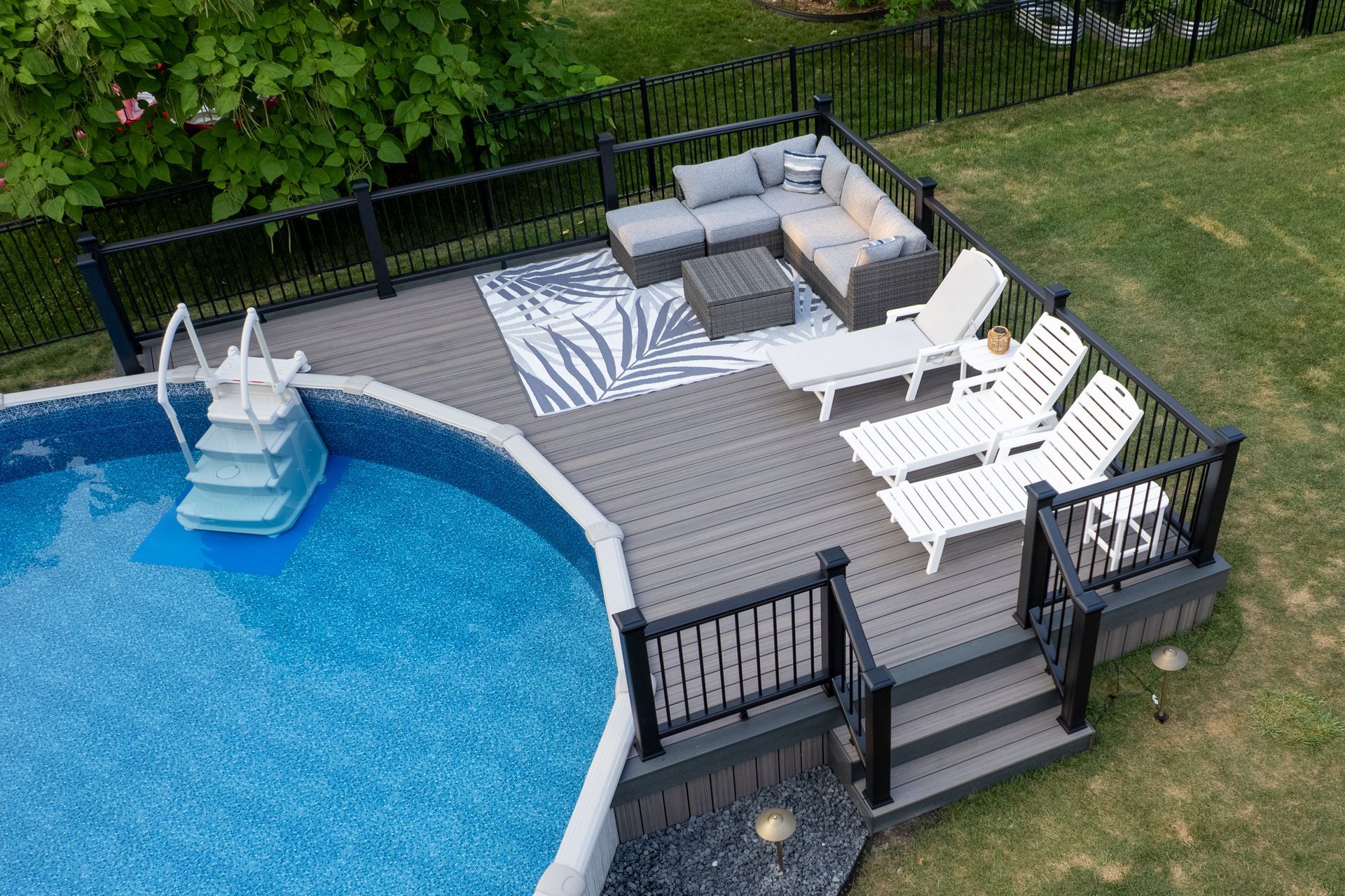 Deck with pool, sectional sofa, and lounge chairs. Grey deck, black railing, blue pool.