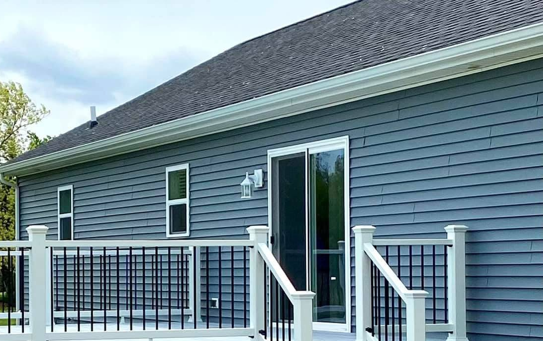 Blue house exterior with deck, sliding glass door, white trim, and black railing.