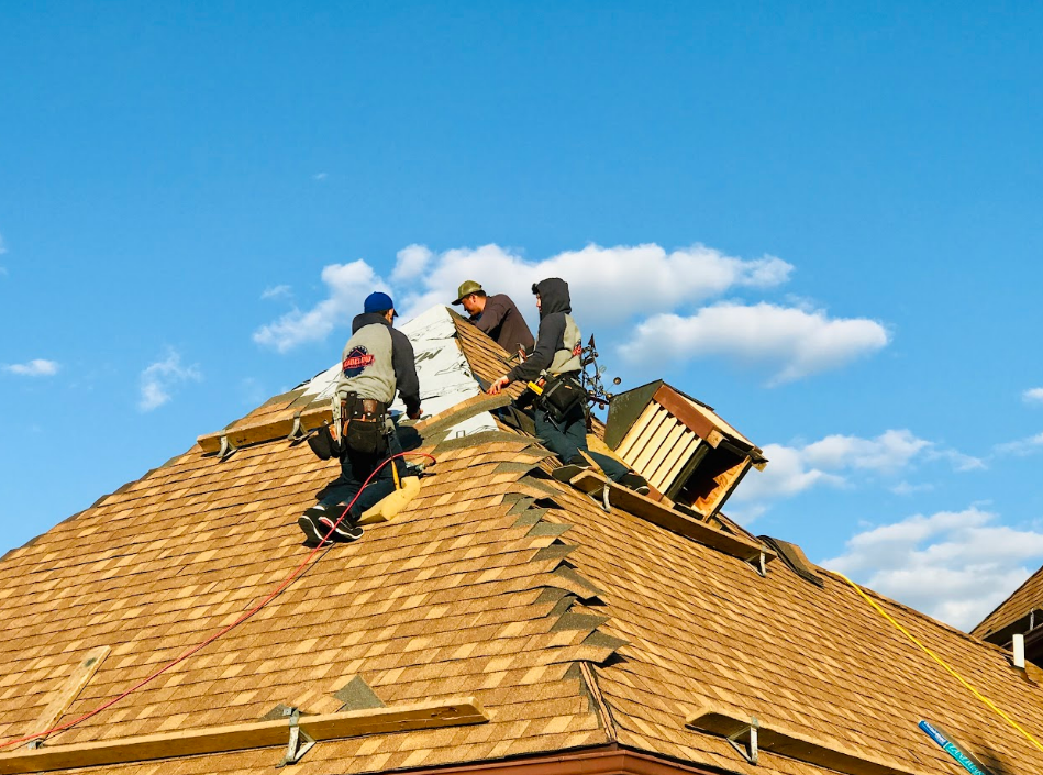 Roofers installing shingles on a house roof under a blue sky.