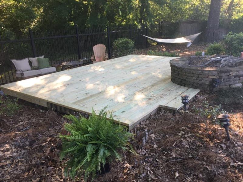 A wooden deck is sitting in the middle of a backyard.