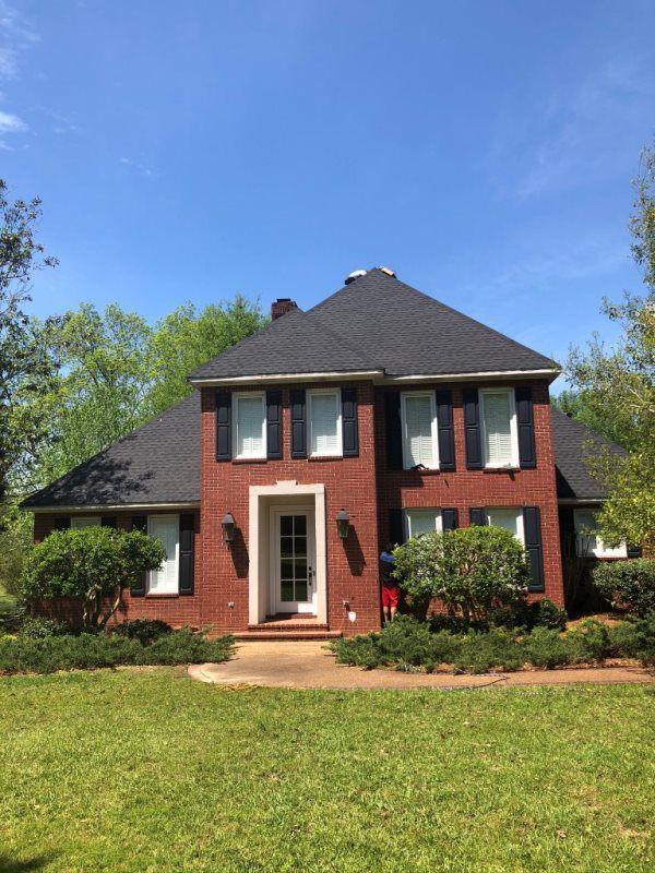 A large brick house with a black roof and black shutters is sitting on top of a lush green lawn.