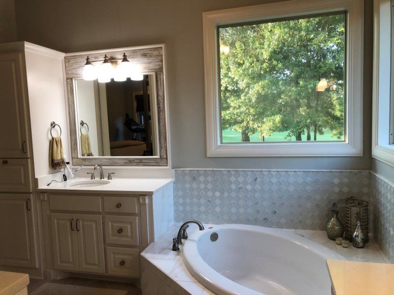 A bathroom with a tub , sink , mirror and window.