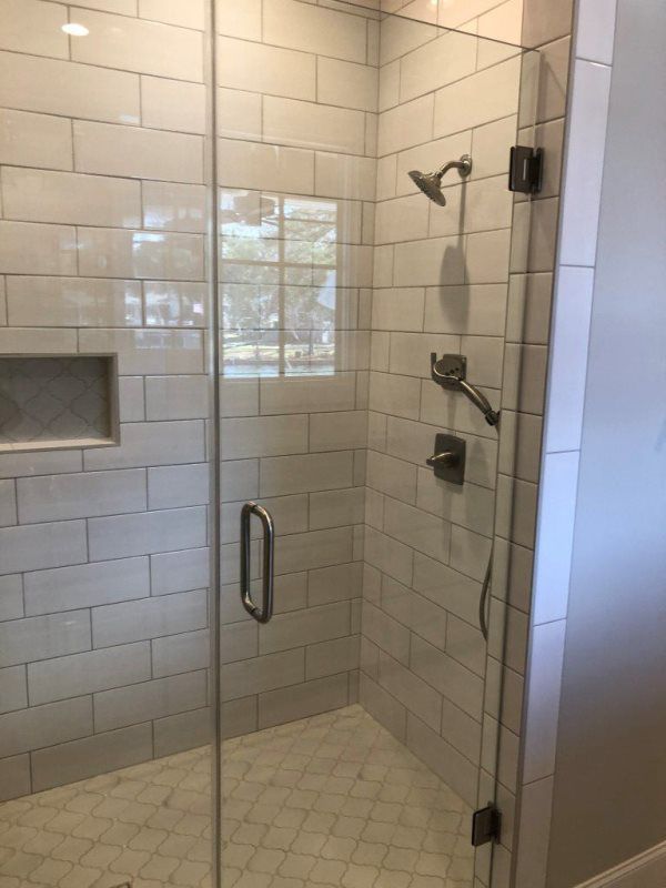 A walk in shower with a glass door and white tiles.