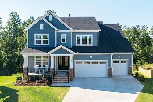 A large blue house with a black roof and white trim is sitting on top of a lush green hillside.