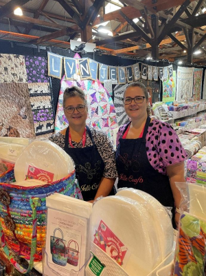 Two Women Smiling Behind Colorful Quilt Displays — Lyn-Jelle Crafts in Emu Park, QLD