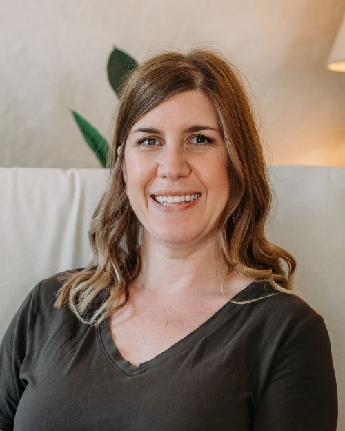 A woman in a blue shirt is smiling in front of a tree
