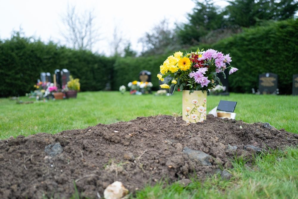 A vase of flowers is sitting on top of a grave in a cemetery.