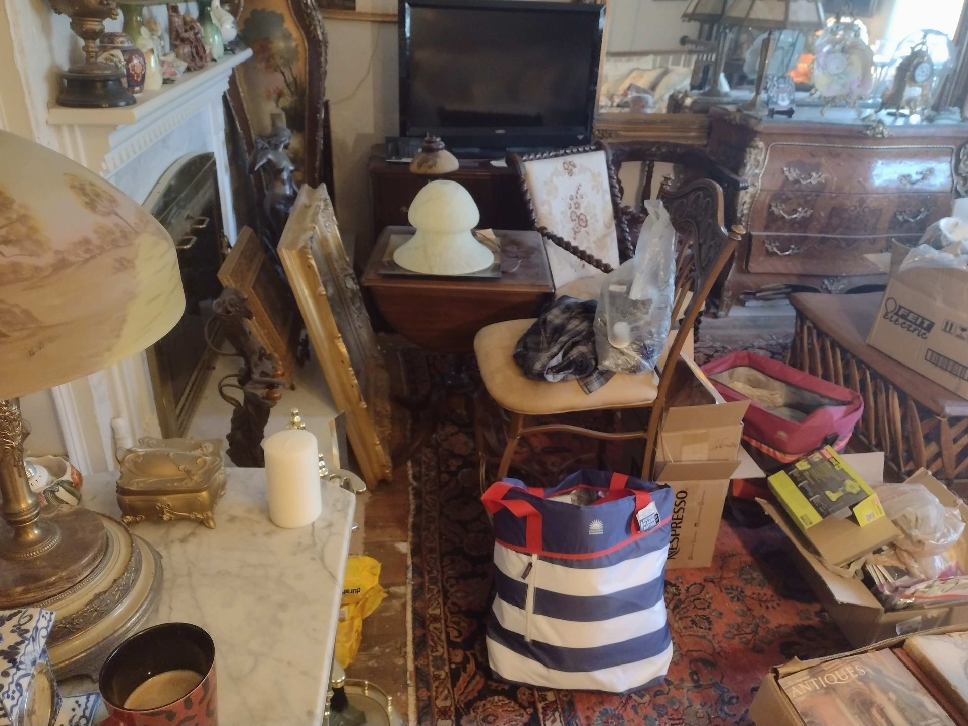 Cluttered room with furniture, decor, a television, and assorted items, including a bag and boxes.
