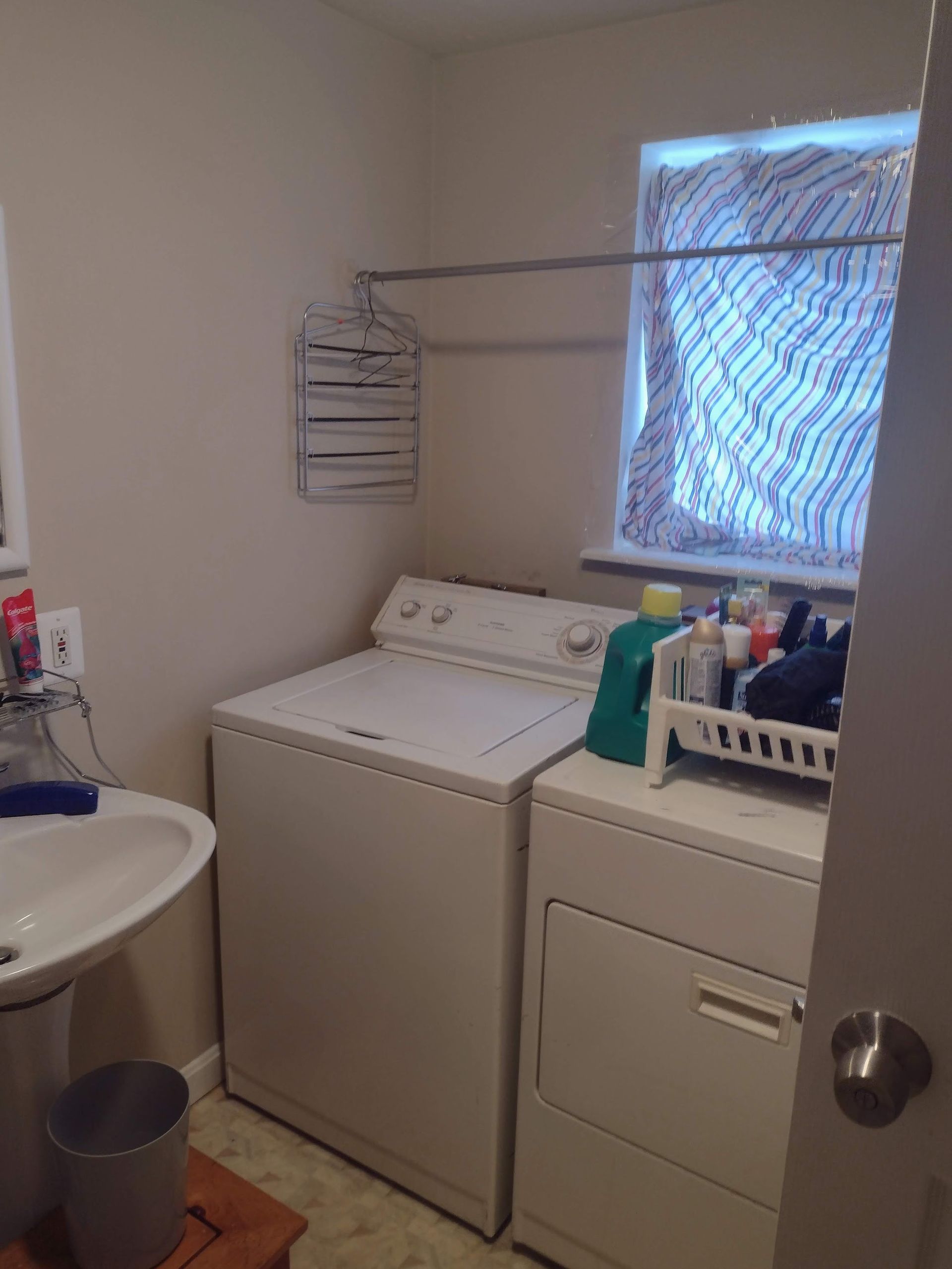 Laundry room with a washing machine, dryer, sink, window, and drying rack.