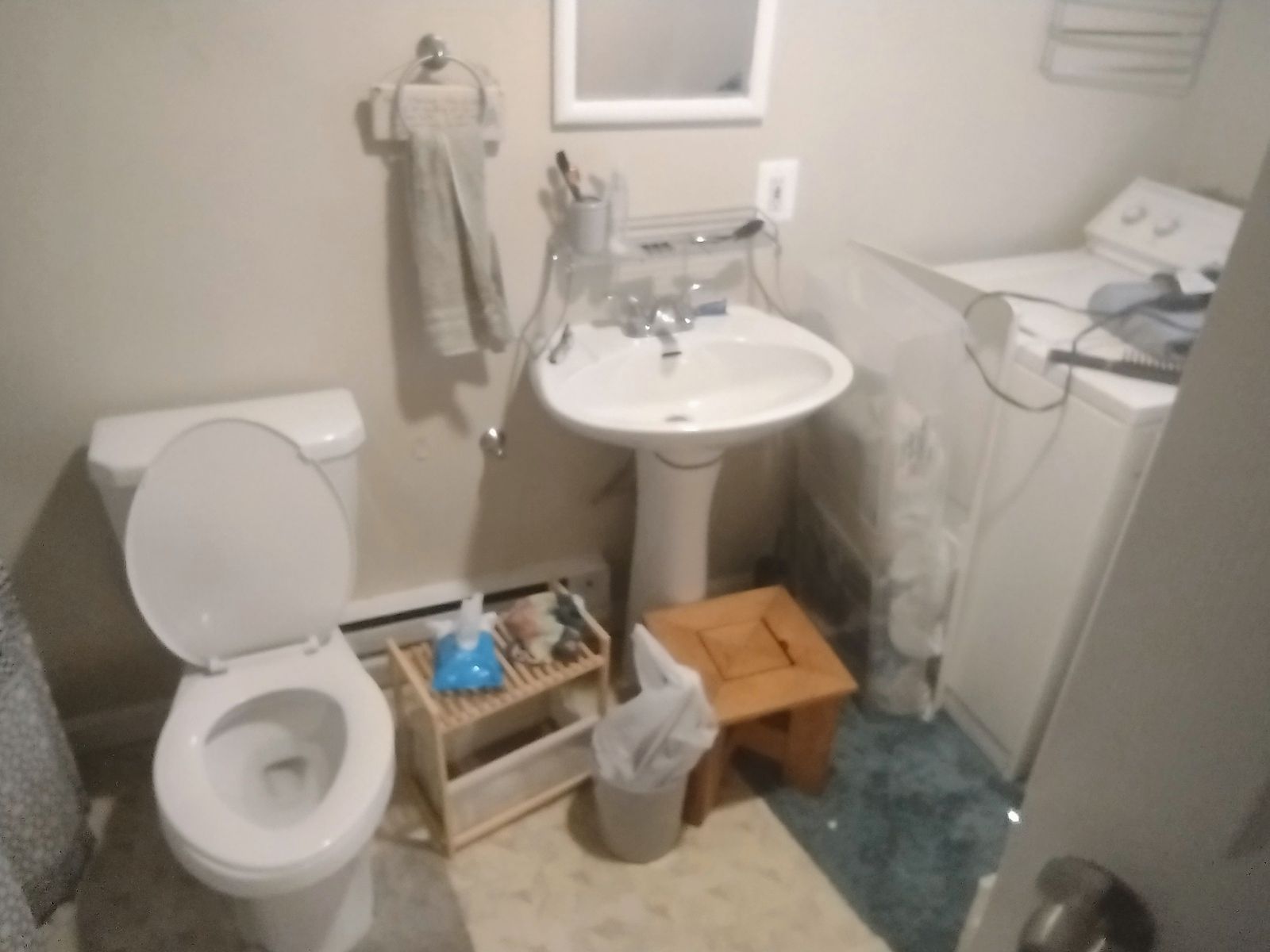 Bathroom with toilet, pedestal sink, and washing machine. Light walls, towel, and stool.