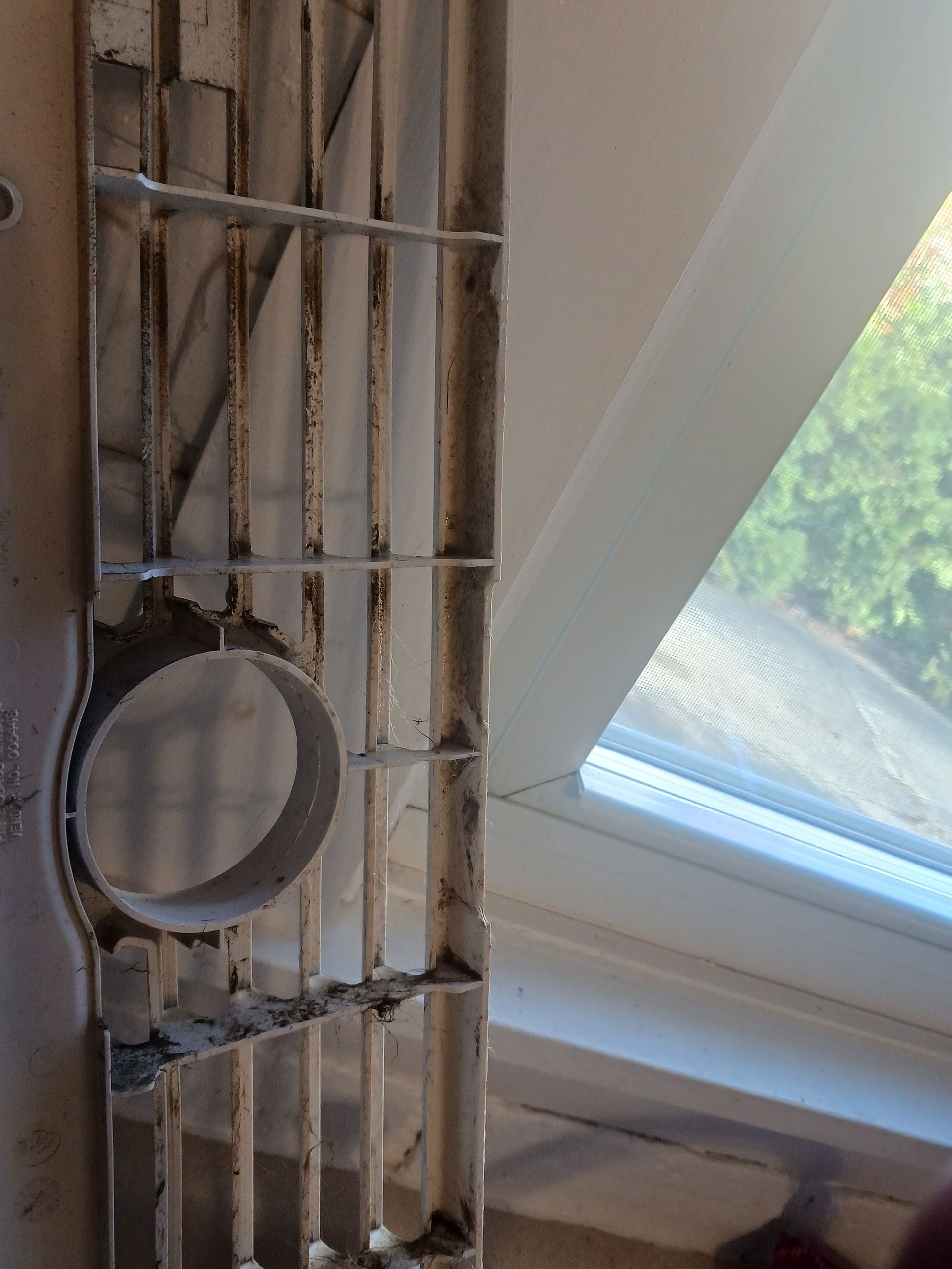 Close-up of a vent with a circular opening, near a white window frame, and dirty.
