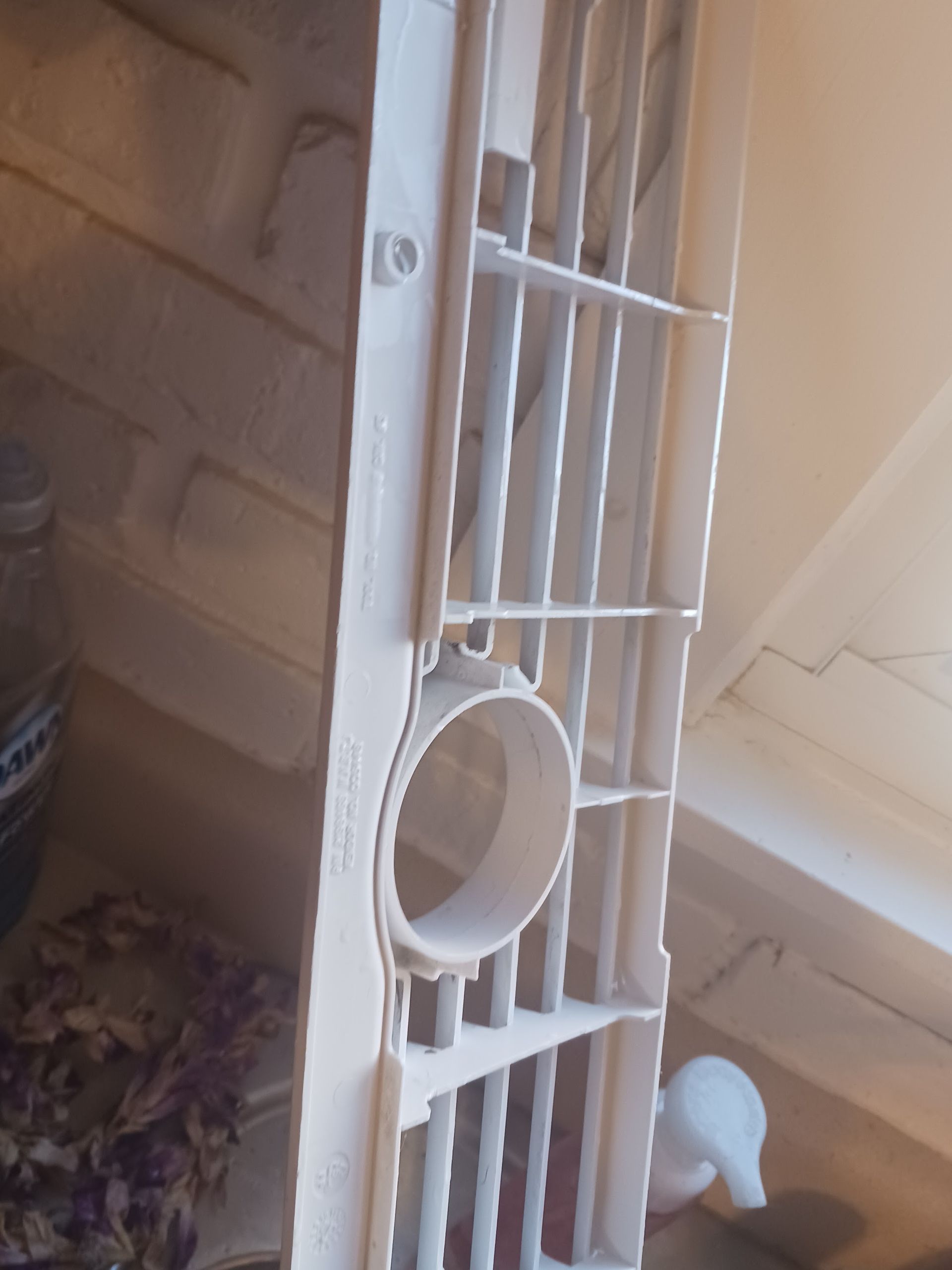 White plastic air vent with a circular opening, set against a wooden wall.