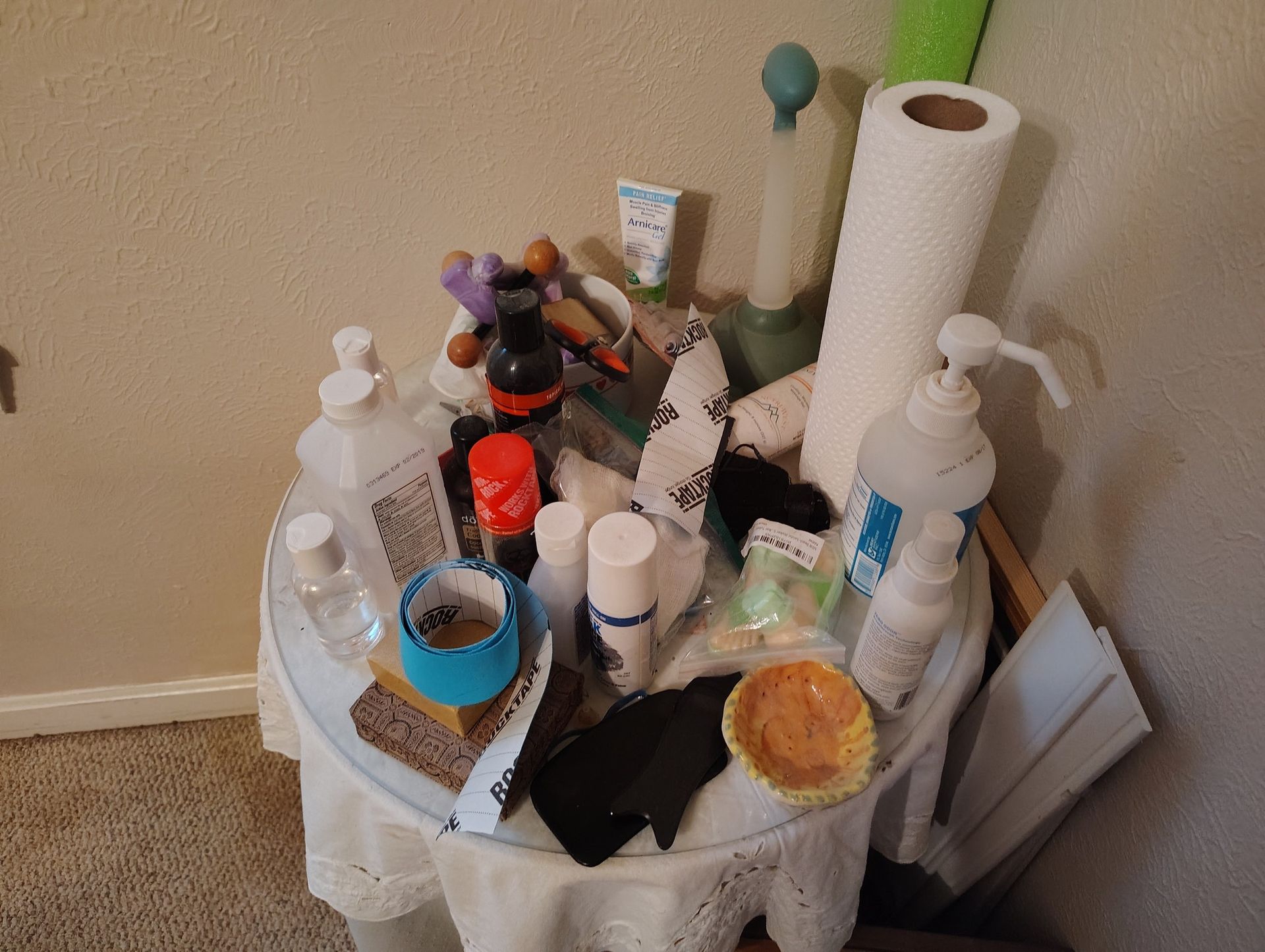 A round table crowded with various bottles, rolls of paper towels, and other personal items.