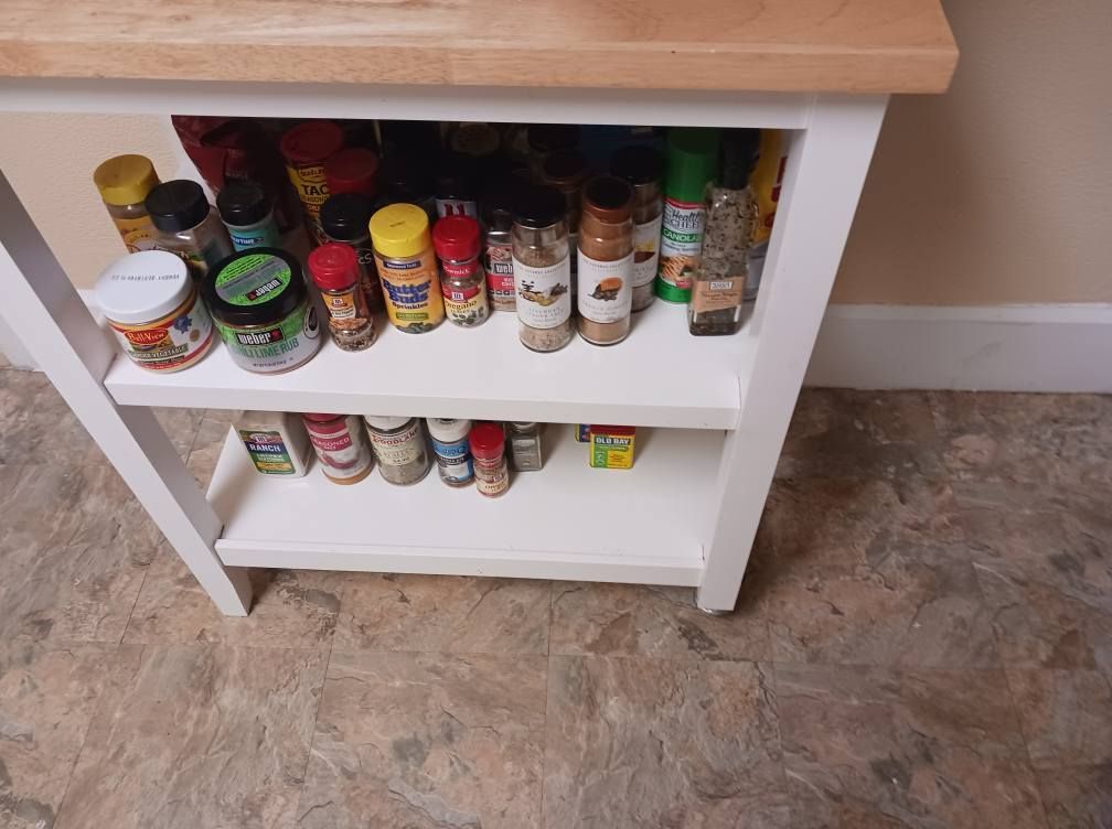 A kitchen island with a light wooden top and white shelves holding various spice jars.