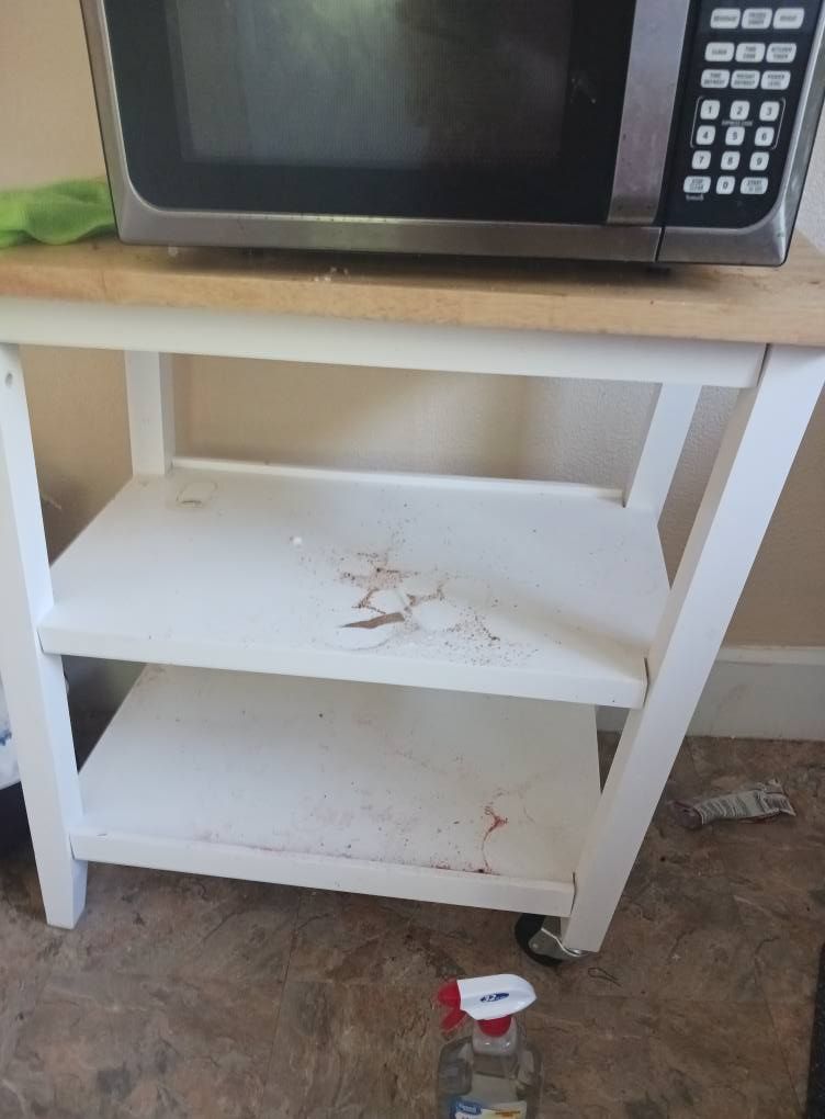 White microwave cart with microwave on top and stains on shelves.