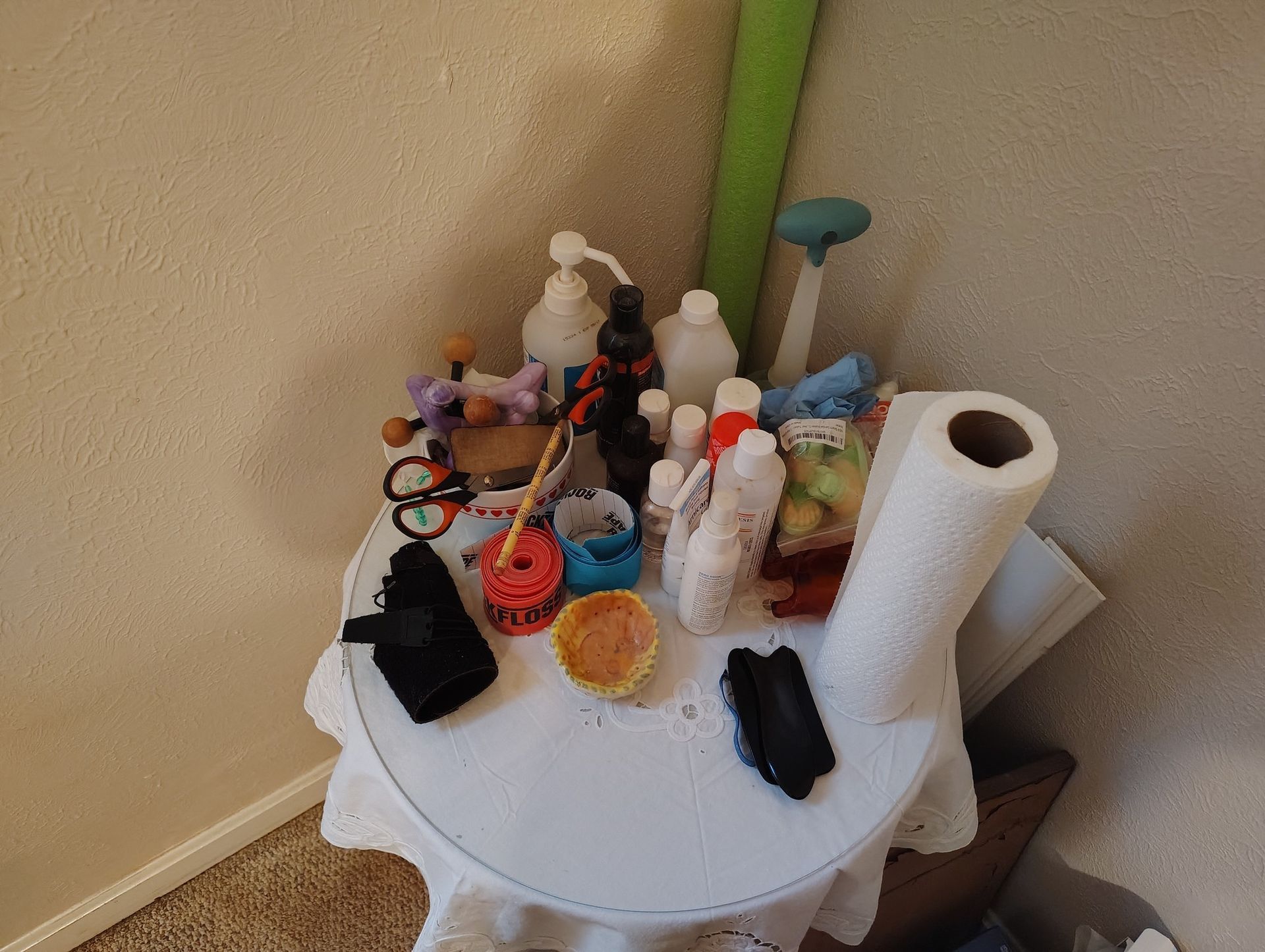 A cluttered white table in a corner, with various objects including bottles, a paper towel roll, and a sponge.