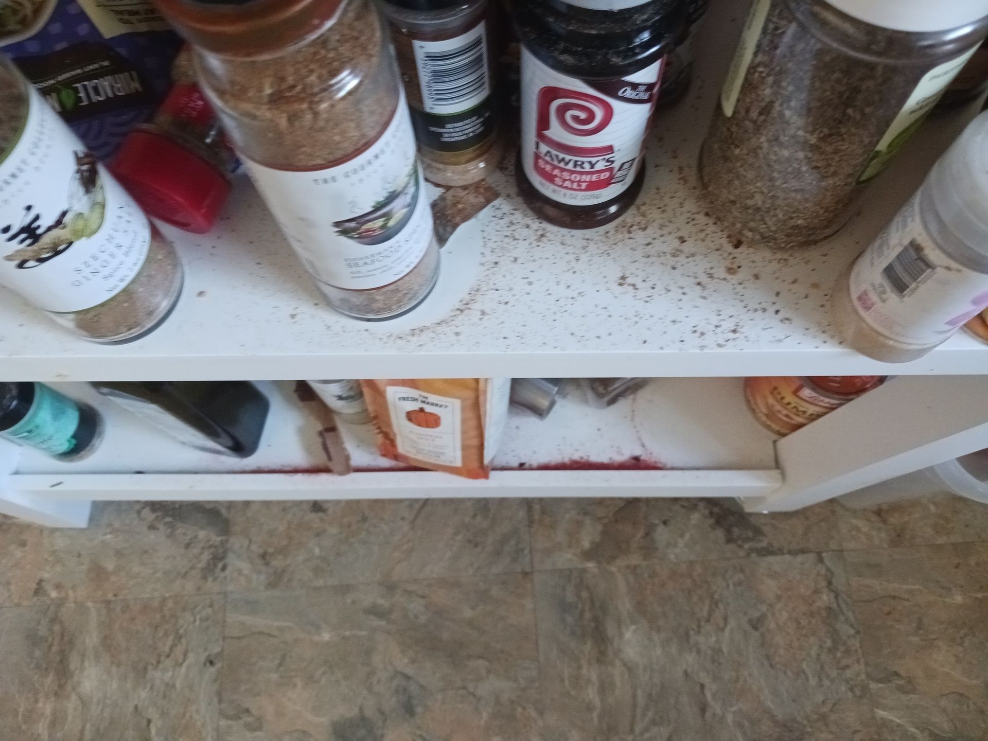 Spice rack with various jars on a white shelf, some spilled spices.