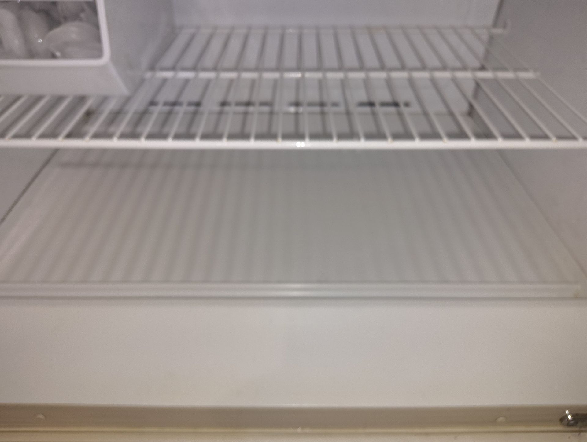 Empty refrigerator interior with wire shelves and a solid bottom shelf.