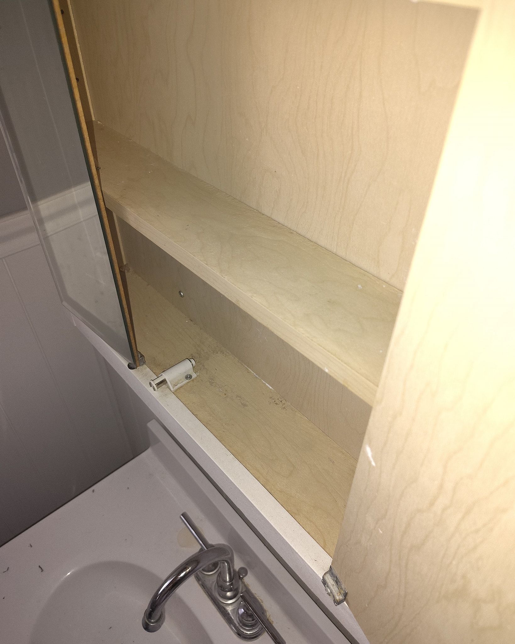 Inside of an open, empty medicine cabinet above a bathroom sink. Beige shelves are visible.
