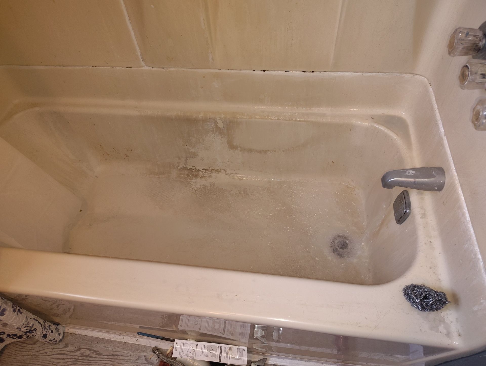 A dirty bathtub with soap scum and grime. Beige color, filled with some water.