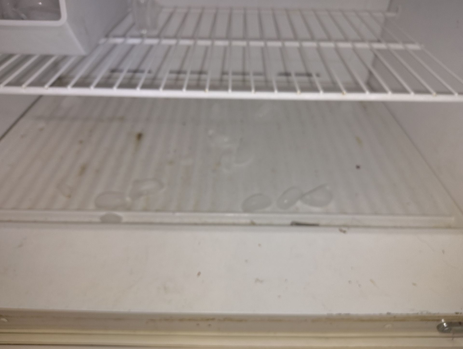 Empty, dirty refrigerator interior with wire shelves and a plastic bottom.