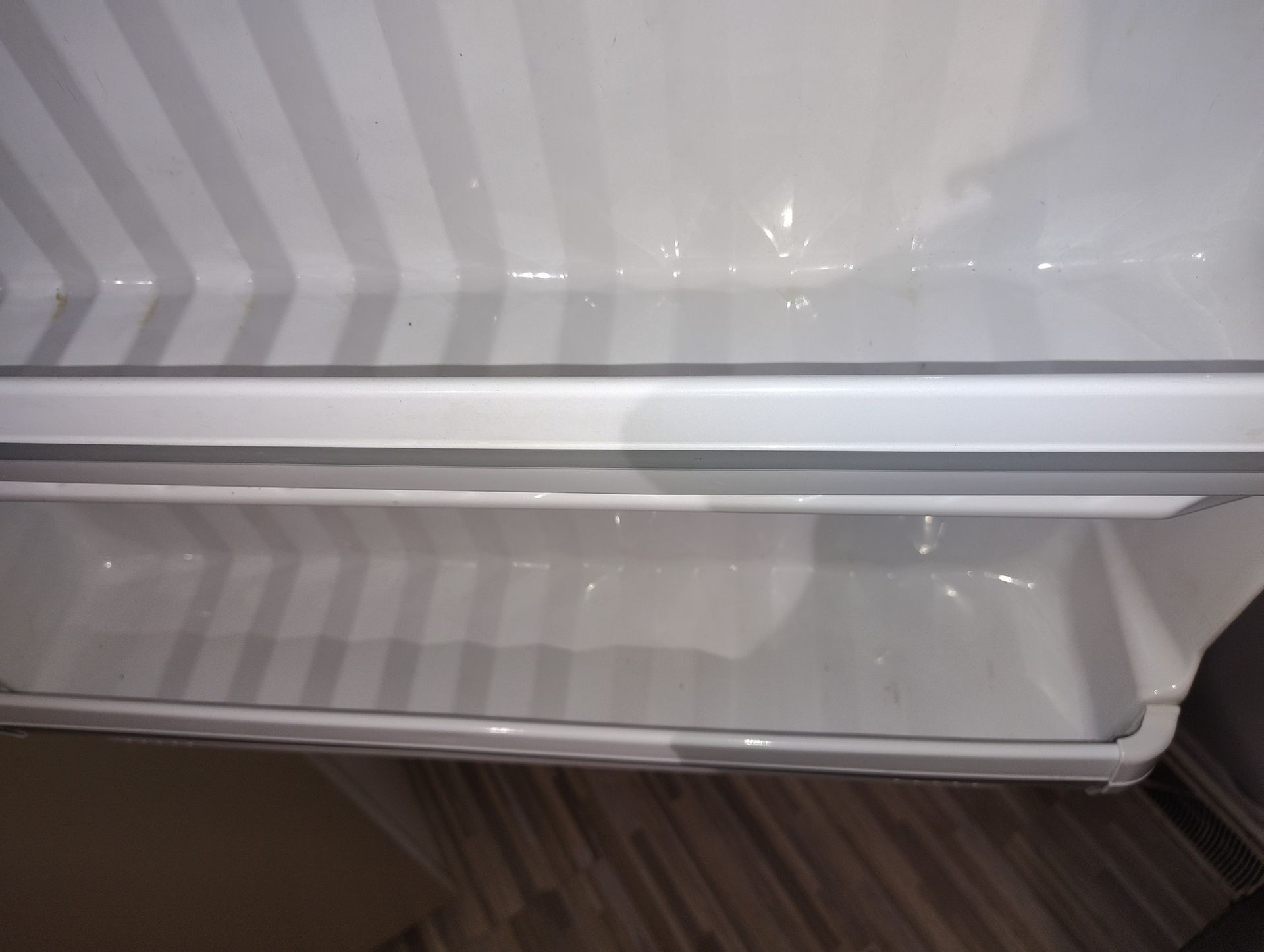 Empty white refrigerator interior with a crisper drawer visible below a shelf.