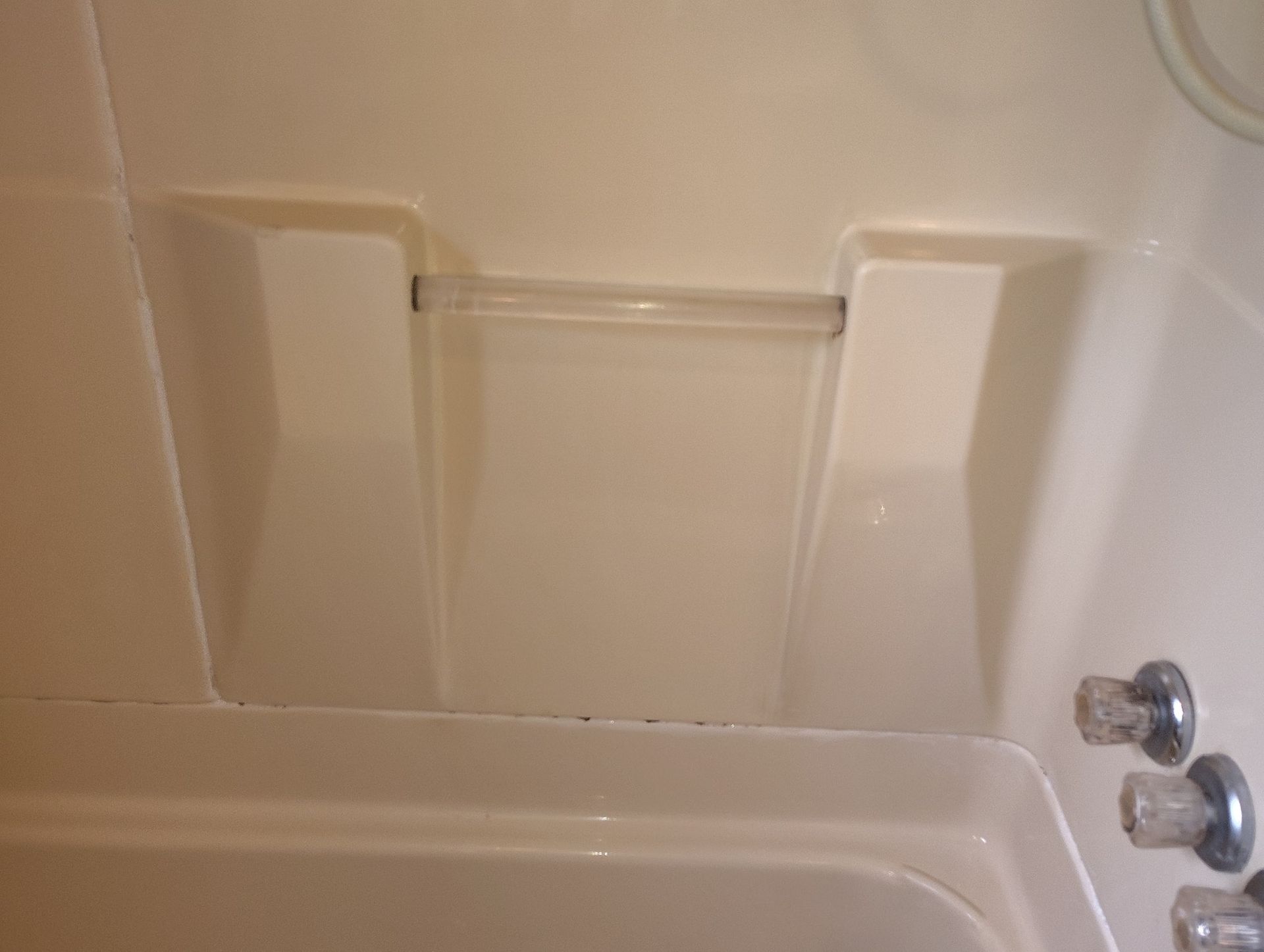 White bathtub with built-in shelf and shower controls on right.