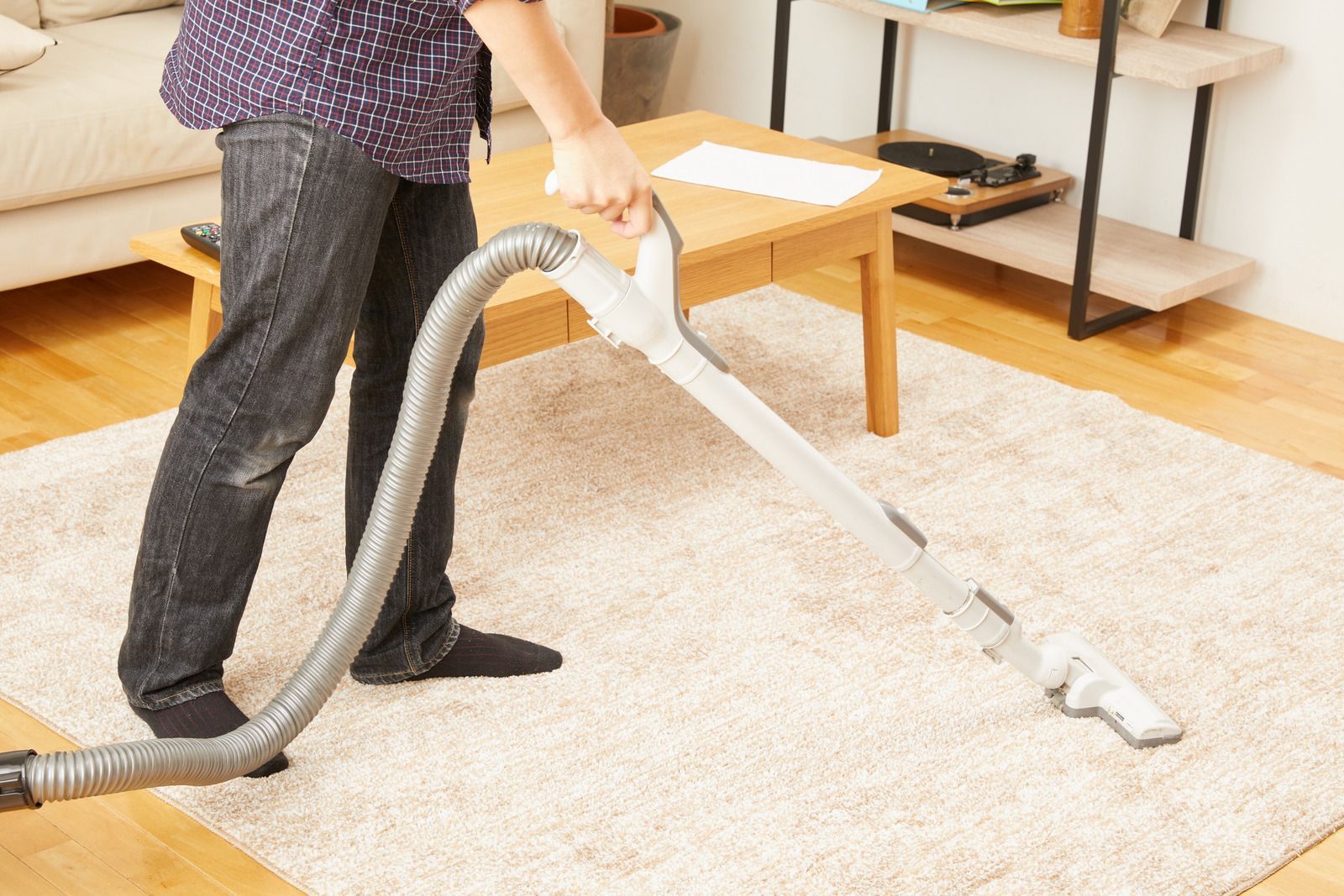 Person vacuuming a light-colored rug with a vacuum cleaner.